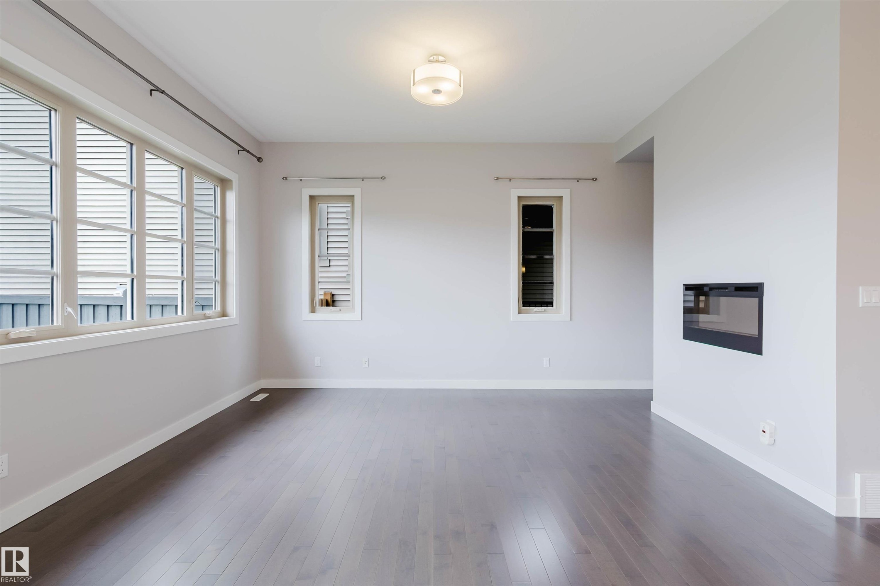 Expansive room featuring wood-finish flooring, a contemporary wall-mounted fireplace, multiple windows with white trim, and a flush-mount ceiling light fixture - 2921 Anderson Crest Sw, Edmonton, AB - Indoor Photo Showing Other Room