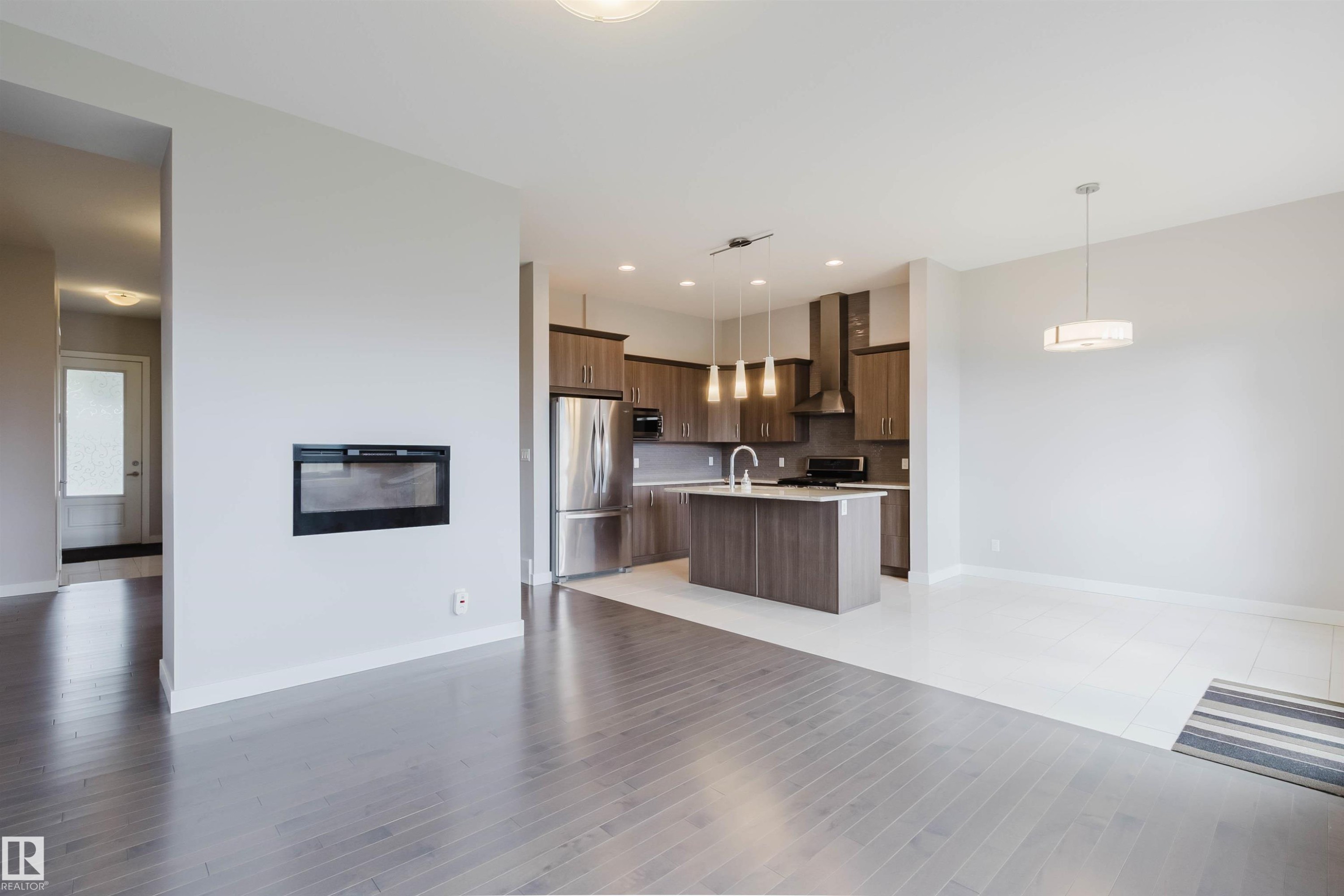 Contemporary open concept living area featuring a built-in electric fireplace, wood-finish flooring, a kitchen island with pendant lighting, stainless steel appliances, and sleek cabinetry - 2921 Anderson Crest Sw, Edmonton, AB - Indoor Photo Showing Kitchen