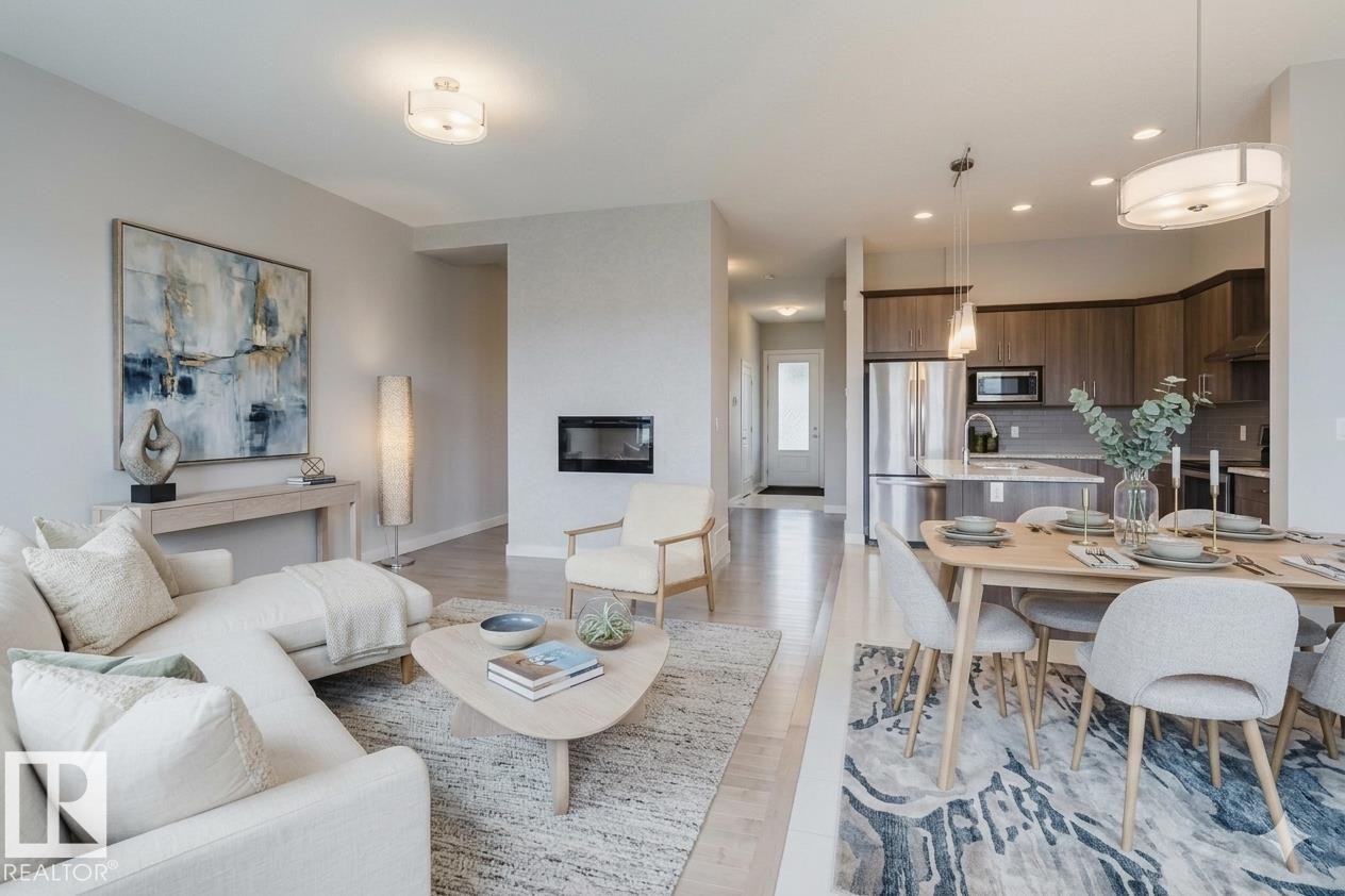 Open-concept living area featuring light wood-finish flooring, a built-in electric fireplace, and a modern kitchen with wood cabinetry, stainless steel appliances, and a central island - 2921 Anderson Crest Sw, Edmonton, AB - Indoor Photo Showing Other Room