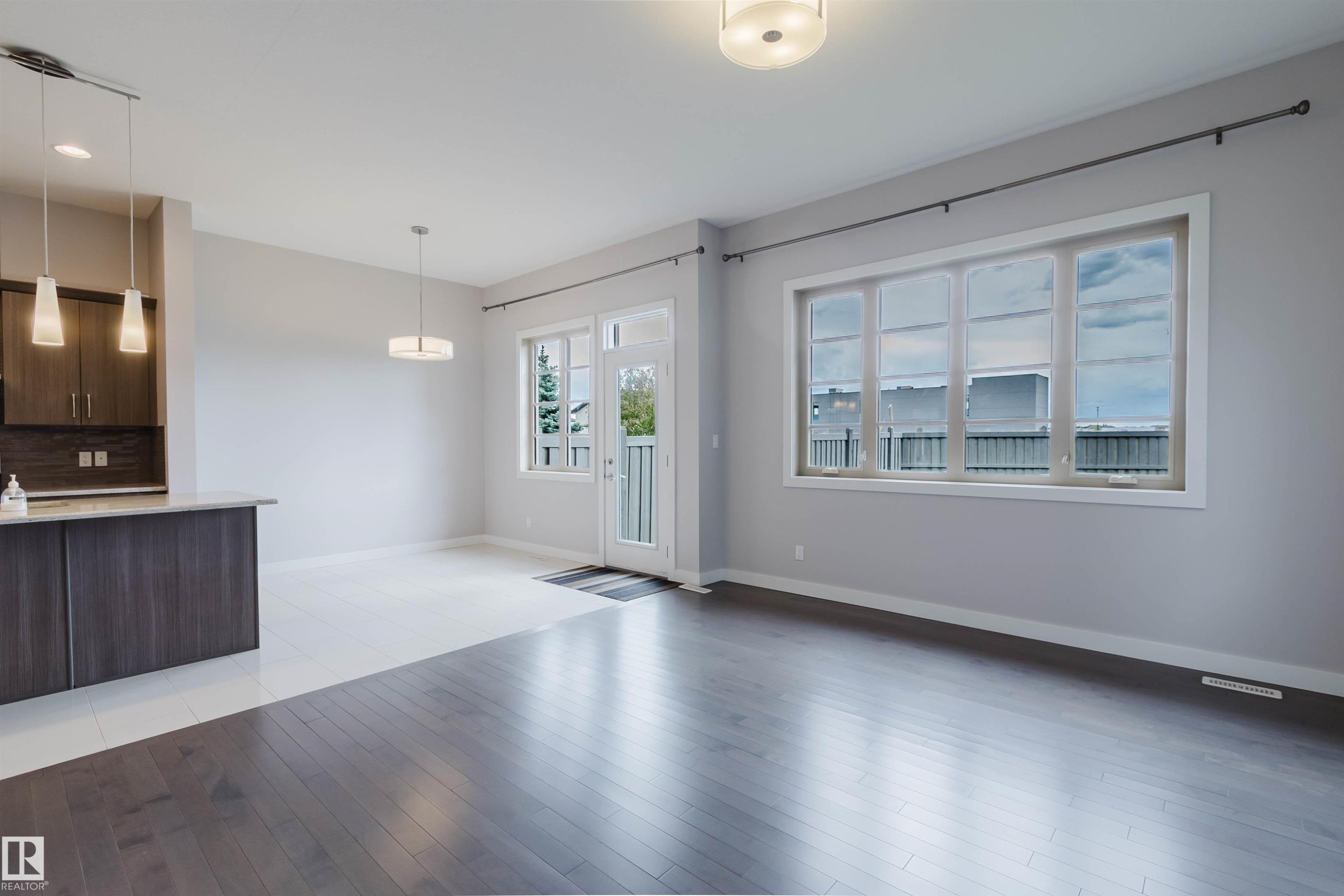 Spacious open-concept living area featuring dark wood-finish flooring, a large multi-pane window, and a glass-paned exterior door - 2921 Anderson Crest Sw, Edmonton, AB - Indoor