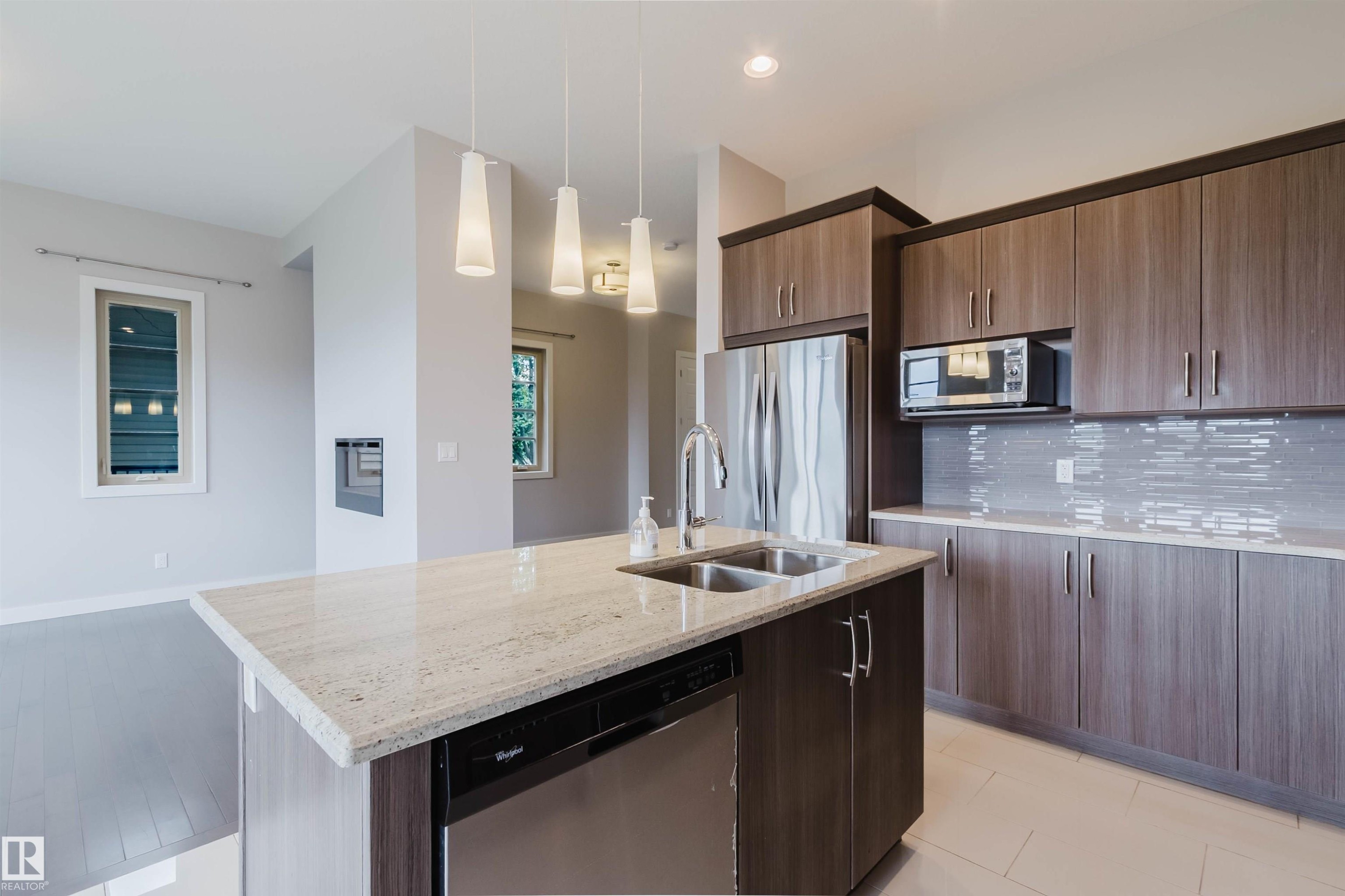 Modern kitchen featuring an island with a double stainless steel sink, a stainless steel dishwasher, and pendant lighting - 2921 Anderson Crest Sw, Edmonton, AB - Indoor Photo Showing Kitchen With Double Sink With Upgraded Kitchen