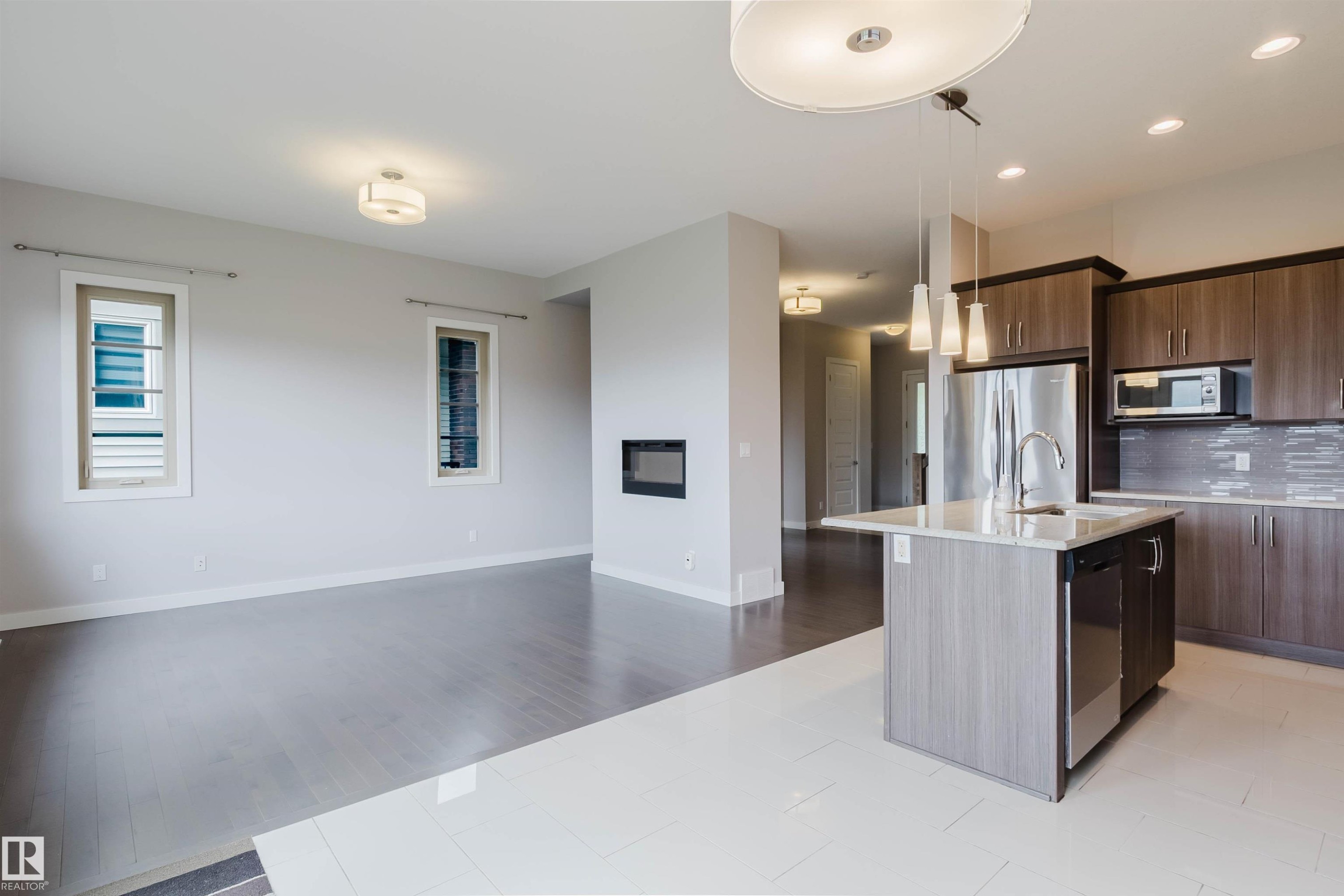 Open concept living area featuring a kitchen island with sink and pendant lighting, stainless steel appliances, wood-finish cabinetry, and a modern fireplace - 2921 Anderson Crest Sw, Edmonton, AB - Indoor Photo Showing Kitchen With Upgraded Kitchen