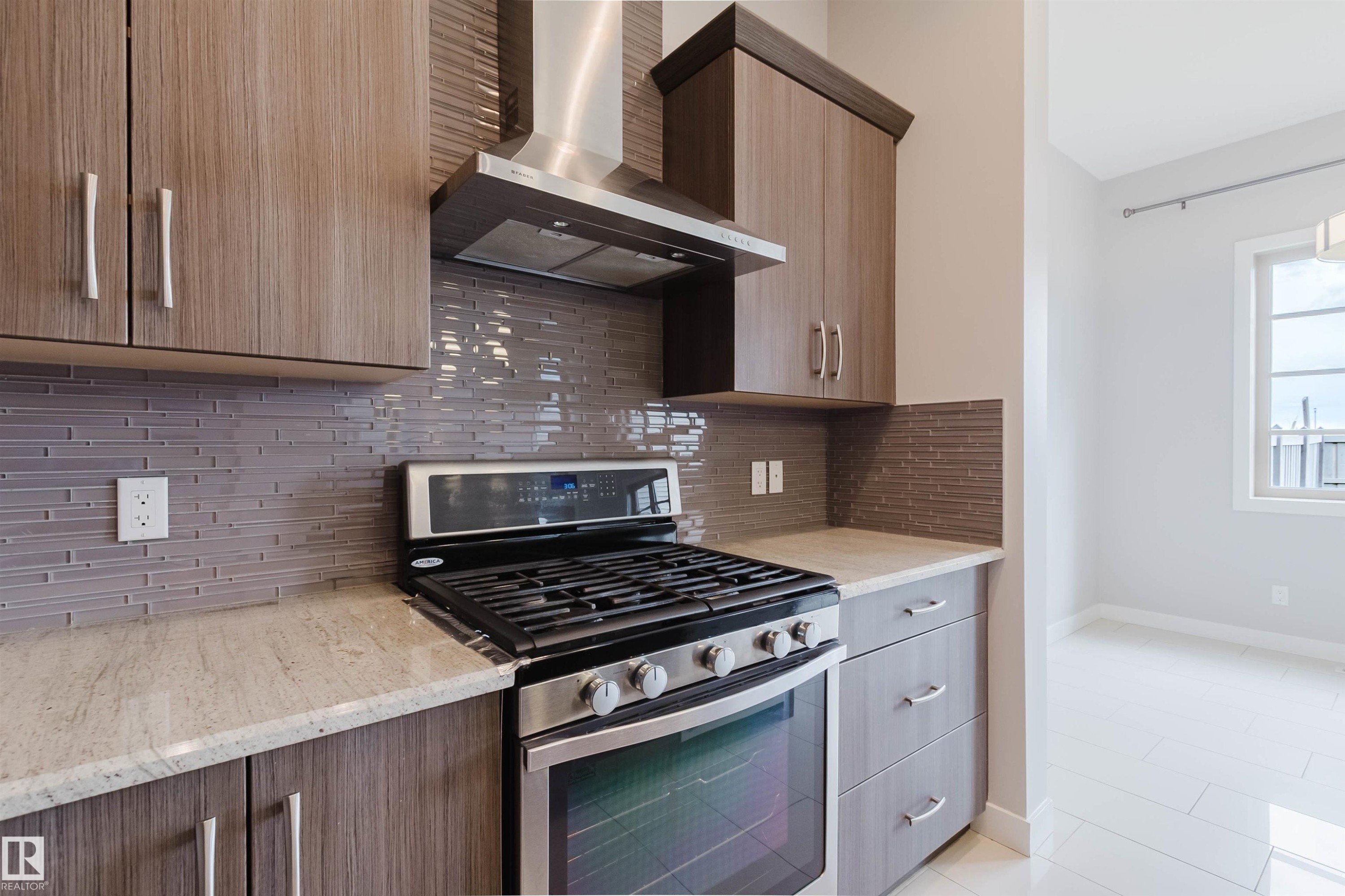 Kitchen showcasing a stainless steel range with a coordinating hood, light-toned countertops, and a gray horizontal tile backsplash - 2921 Anderson Crest Sw, Edmonton, AB - Indoor Photo Showing Kitchen