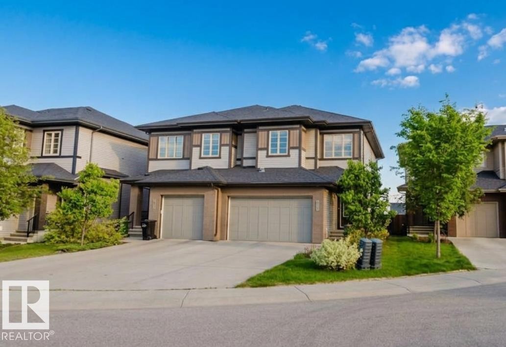 Contemporary townhome featuring a two-car garage, concrete driveway, stone and siding exterior, front yard landscaping, and mature trees - 2921 Anderson Crest Sw, Edmonton, AB - Outdoor With Facade