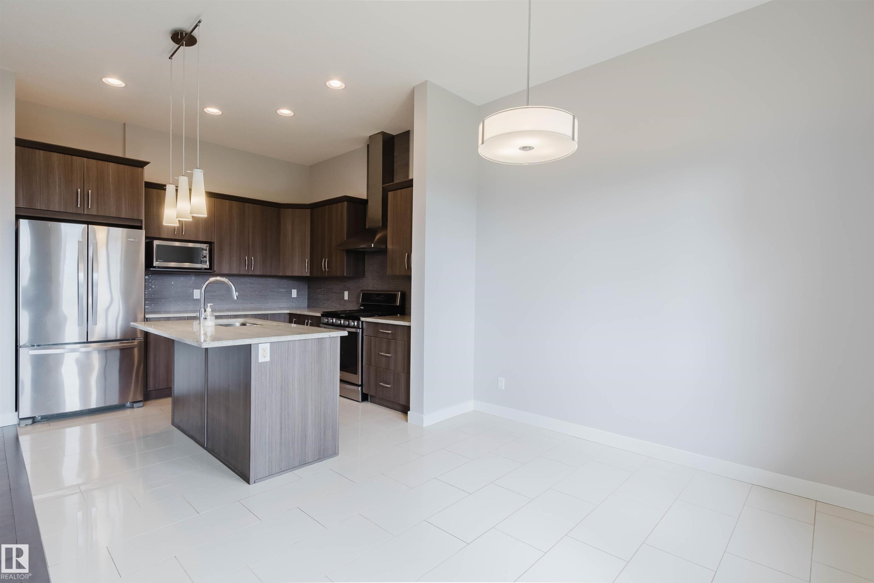 Modern kitchen featuring wood-finish cabinetry, stainless steel appliances, a center island with sink, pendant lighting, and a tile backsplash - 2921 Anderson Crest Sw, Edmonton, AB - Indoor Photo Showing Kitchen