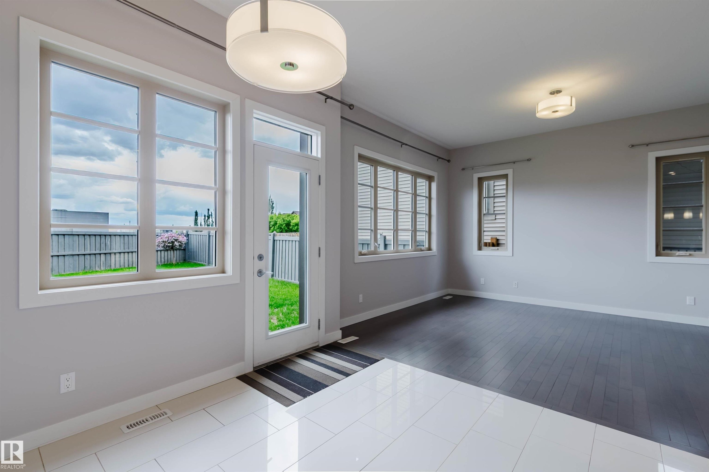 Bright interior space featuring a glass-paned exterior door, multiple windows with white trim, a large surface-mounted drum light fixture, and a combination of white tile and dark wood-finish flooring - 2921 Anderson Crest Sw, Edmonton, AB - Indoor Photo Showing Other Room