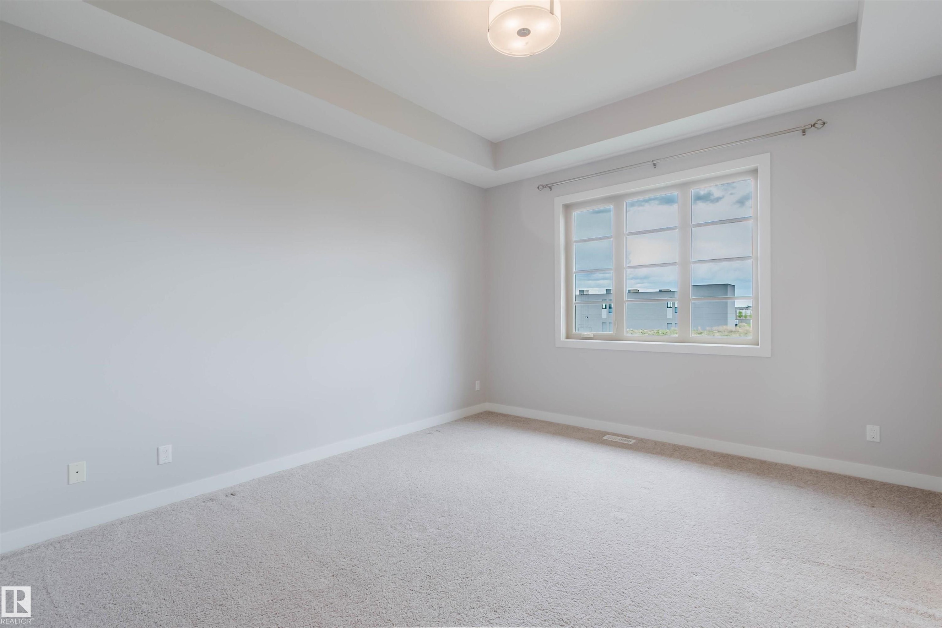 Spacious room featuring light gray walls, plush carpet flooring, a large multi-pane window, tray ceiling detail, and a modern ceiling light fixture - 2921 Anderson Crest Sw, Edmonton, AB - Indoor Photo Showing Other Room