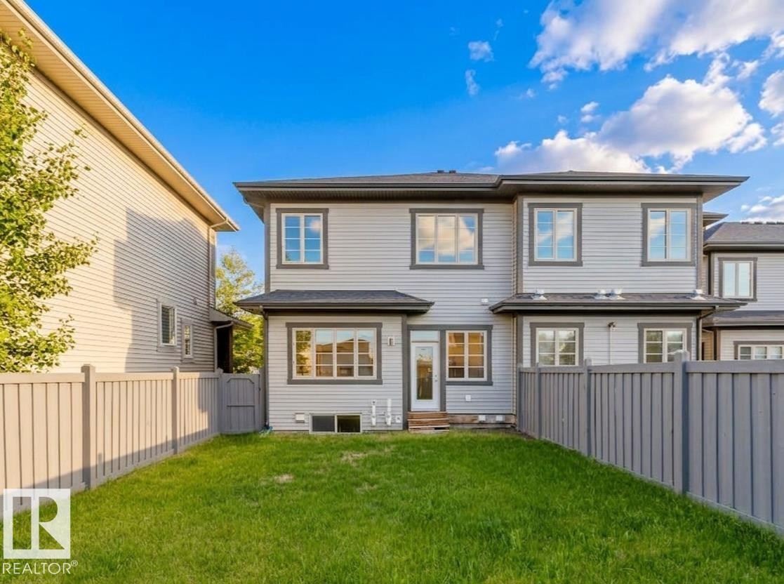 Fenced backyard with a manicured lawn, featuring light gray vinyl siding, dark gray trim, and multiple windows - 2921 Anderson Crest Sw, Edmonton, AB - Outdoor