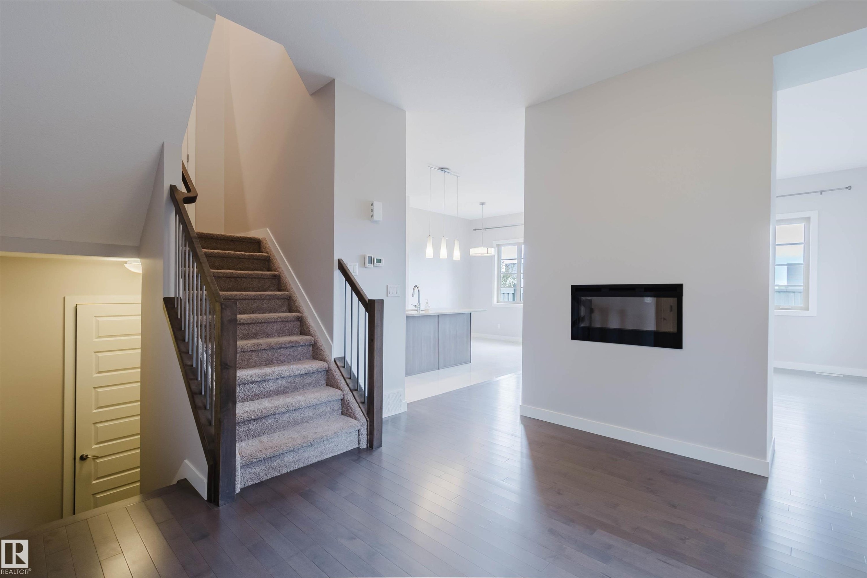 Expansive entry hall featuring wood-finish flooring, a carpeted staircase with wood railing and metal spindles, and a built-in electric fireplace - 2921 Anderson Crest Sw, Edmonton, AB - Indoor With Fireplace