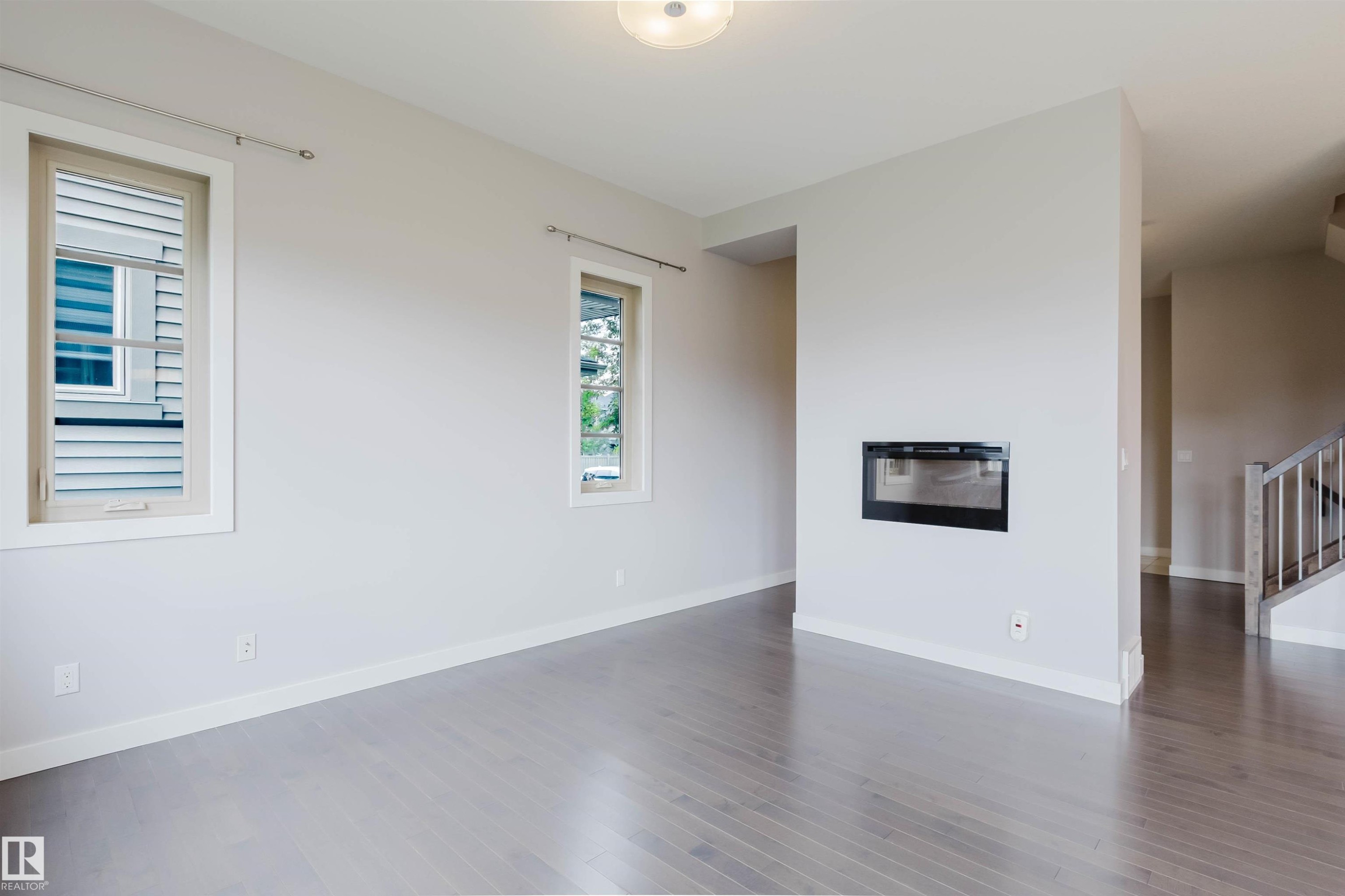 Living area featuring a sleek built-in fireplace, two windows with light-colored frames, wood-finish flooring, and white baseboards - 2921 Anderson Crest Sw, Edmonton, AB - Indoor With Fireplace