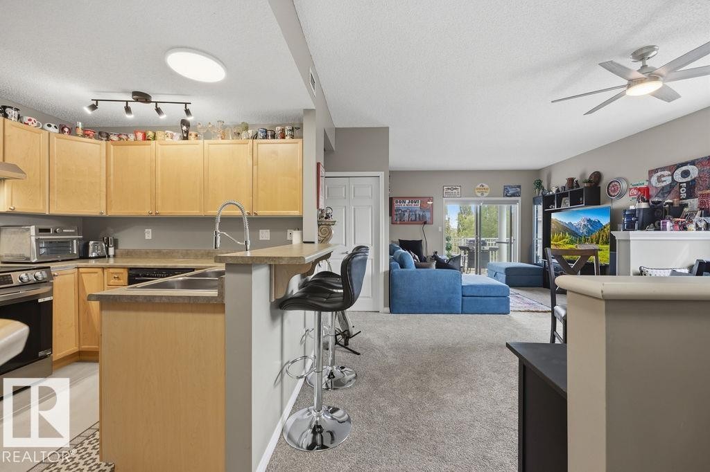 Open-concept kitchen featuring light wood cabinetry, a peninsula with seating, and stainless steel appliances - 71 3040 Spence Wynd, Edmonton, AB