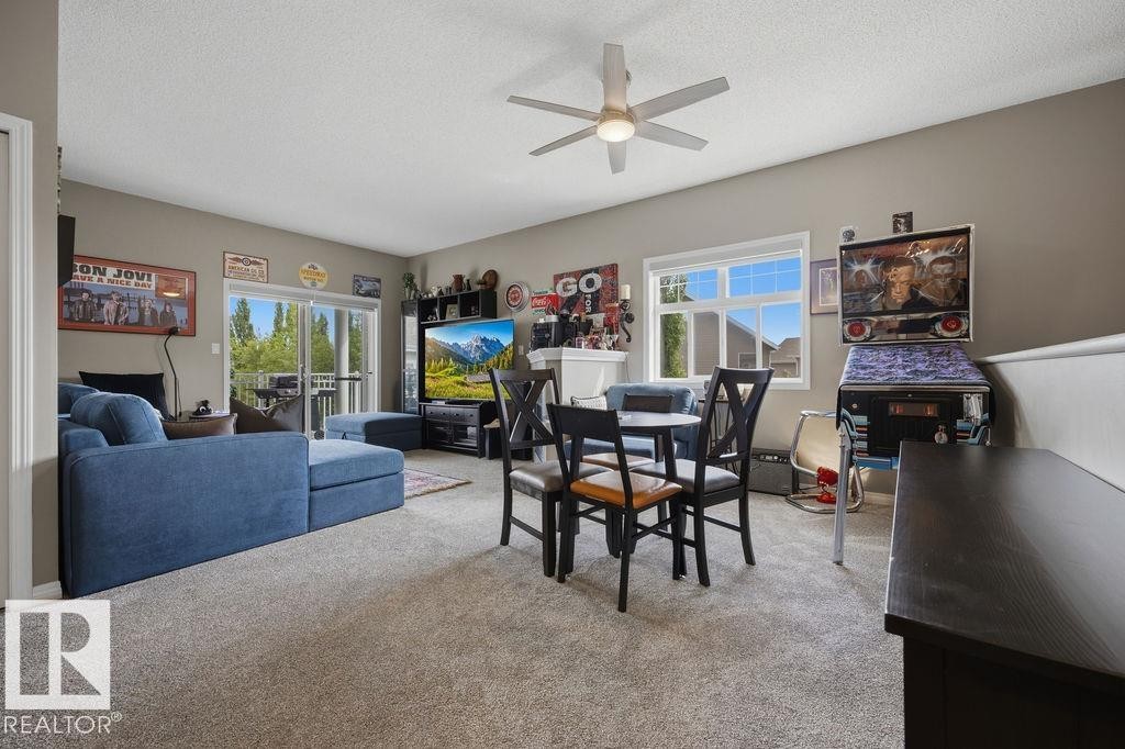 Carpeted living area featuring a ceiling fan, a sliding glass door leading to an outdoor deck, and a white-framed window - 71 3040 Spence Wynd, Edmonton, AB
