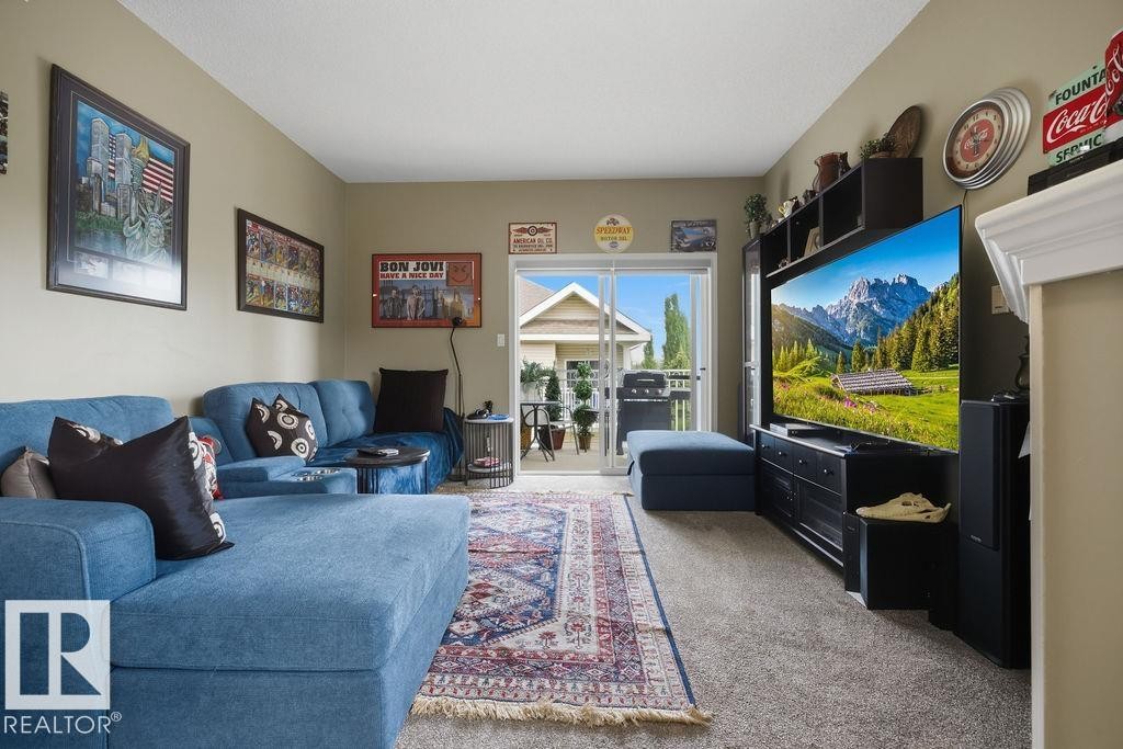 Spacious living area featuring neutral-toned walls, plush carpeting, and a sliding glass door providing natural light and exterior access - 71 3040 Spence Wynd, Edmonton, AB