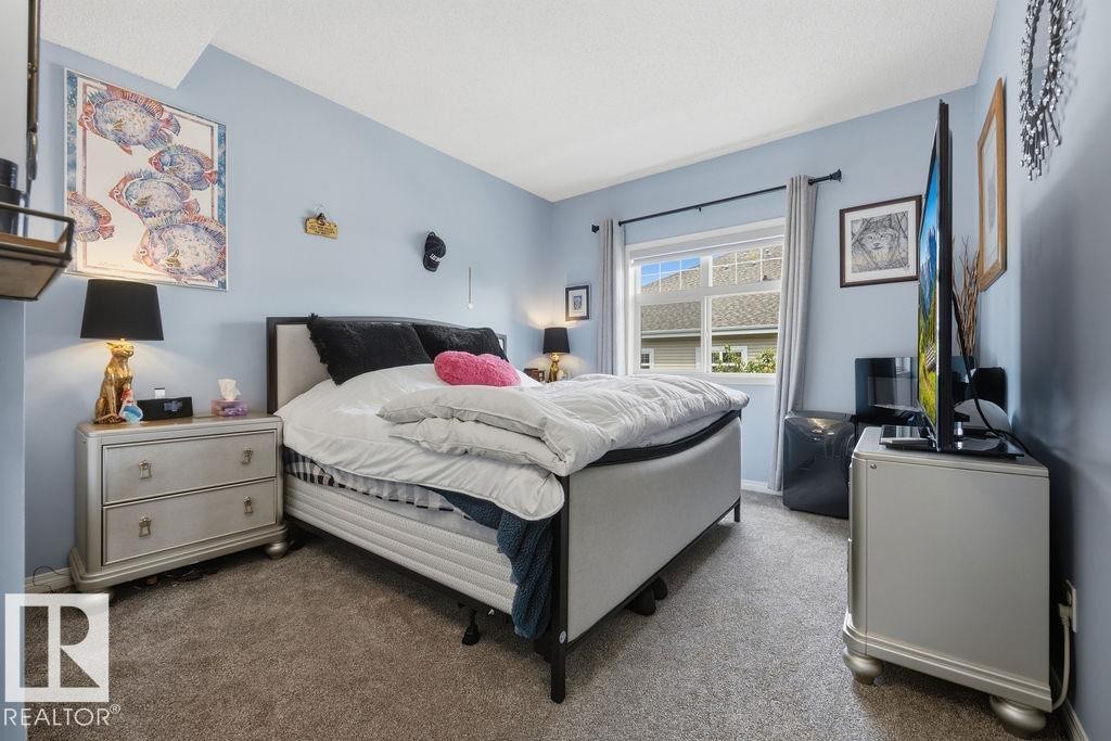 Carpeted bedroom featuring a window with exterior views, light blue wall paint, and a textured ceiling - 71 3040 Spence Wynd, Edmonton, AB