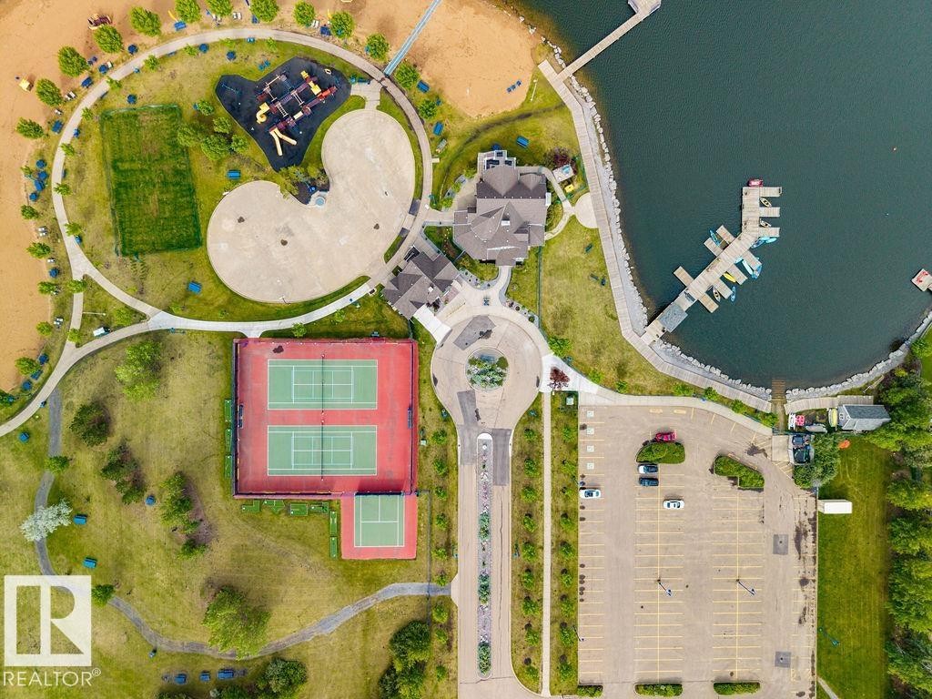 Aerial overview showcasing extensive recreational amenities including a waterfront with boat docks, multiple tennis courts, a playground area, and a large paved parking lot - 71 3040 Spence Wynd, Edmonton, AB