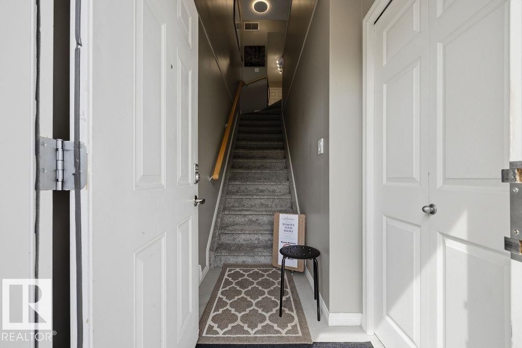 Interior entryway with neutral gray walls, a carpeted staircase, and a light wood-finish handrail - 71 3040 Spence Wynd, Edmonton, AB