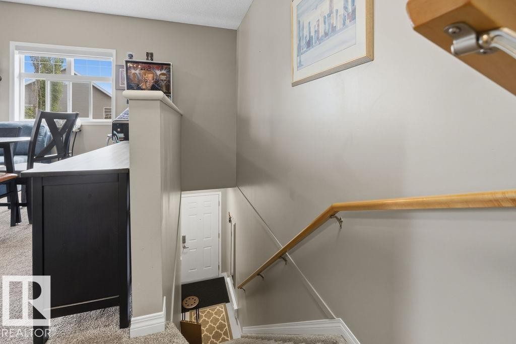 Staircase featuring a light wood-finish handrail, carpeted treads, and neutral wall tones - 71 3040 Spence Wynd, Edmonton, AB