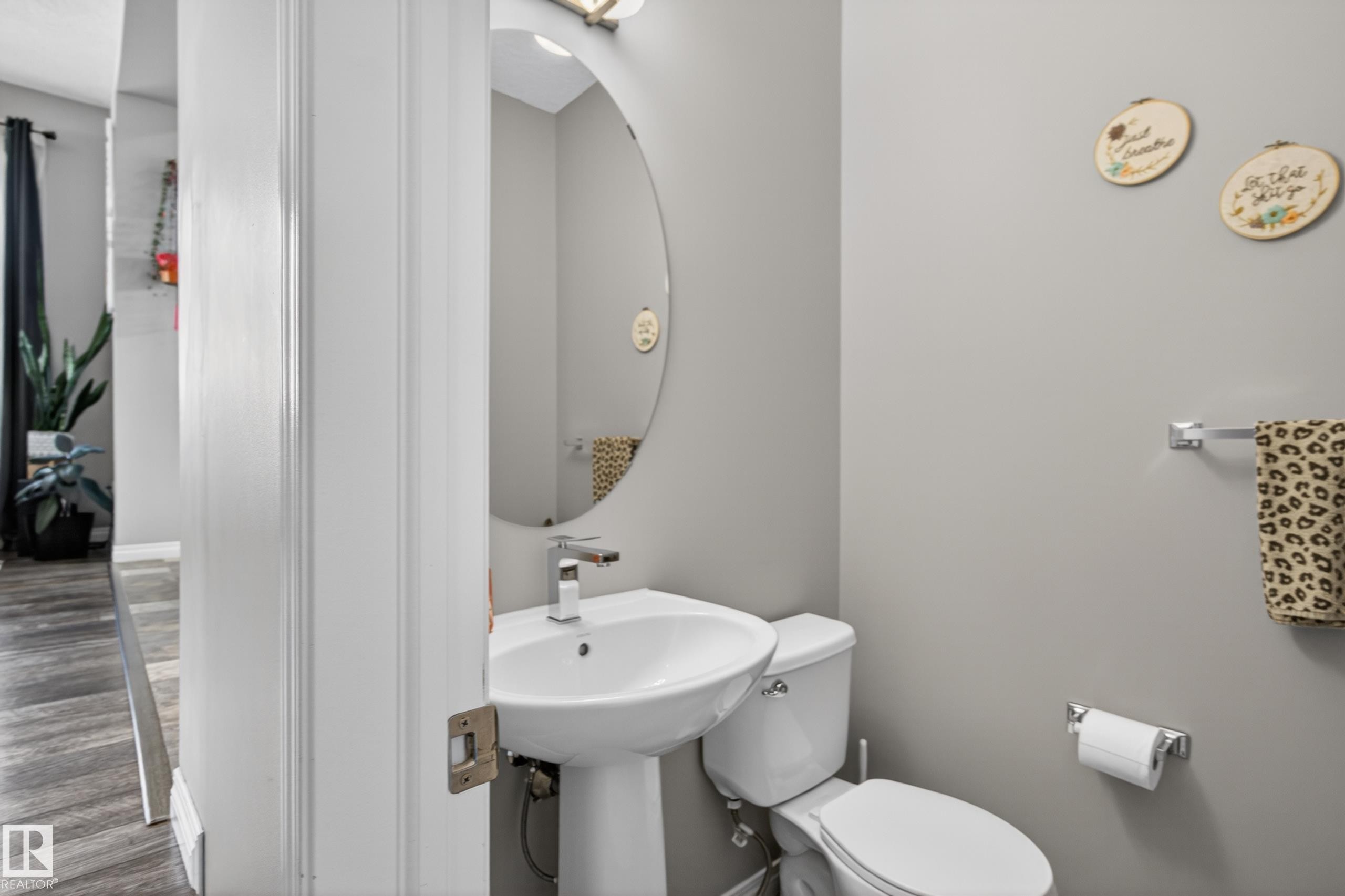 Compact powder room featuring a pedestal sink, a contemporary faucet, and a wall-mounted oval mirror - 9847 220 Street, Edmonton, AB