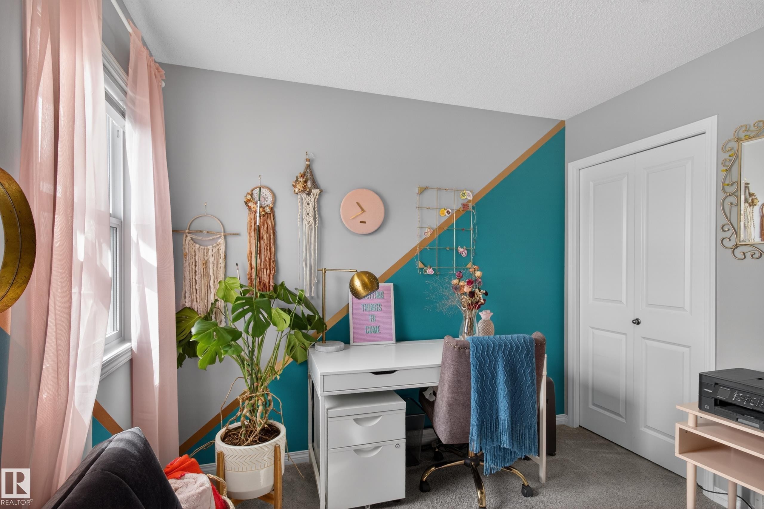 Bright room featuring a window with sheer pink drapes, dual-tone wall paint with a teal accent, white bi-fold closet doors, and light gray carpet flooring - 9847 220 Street, Edmonton, AB