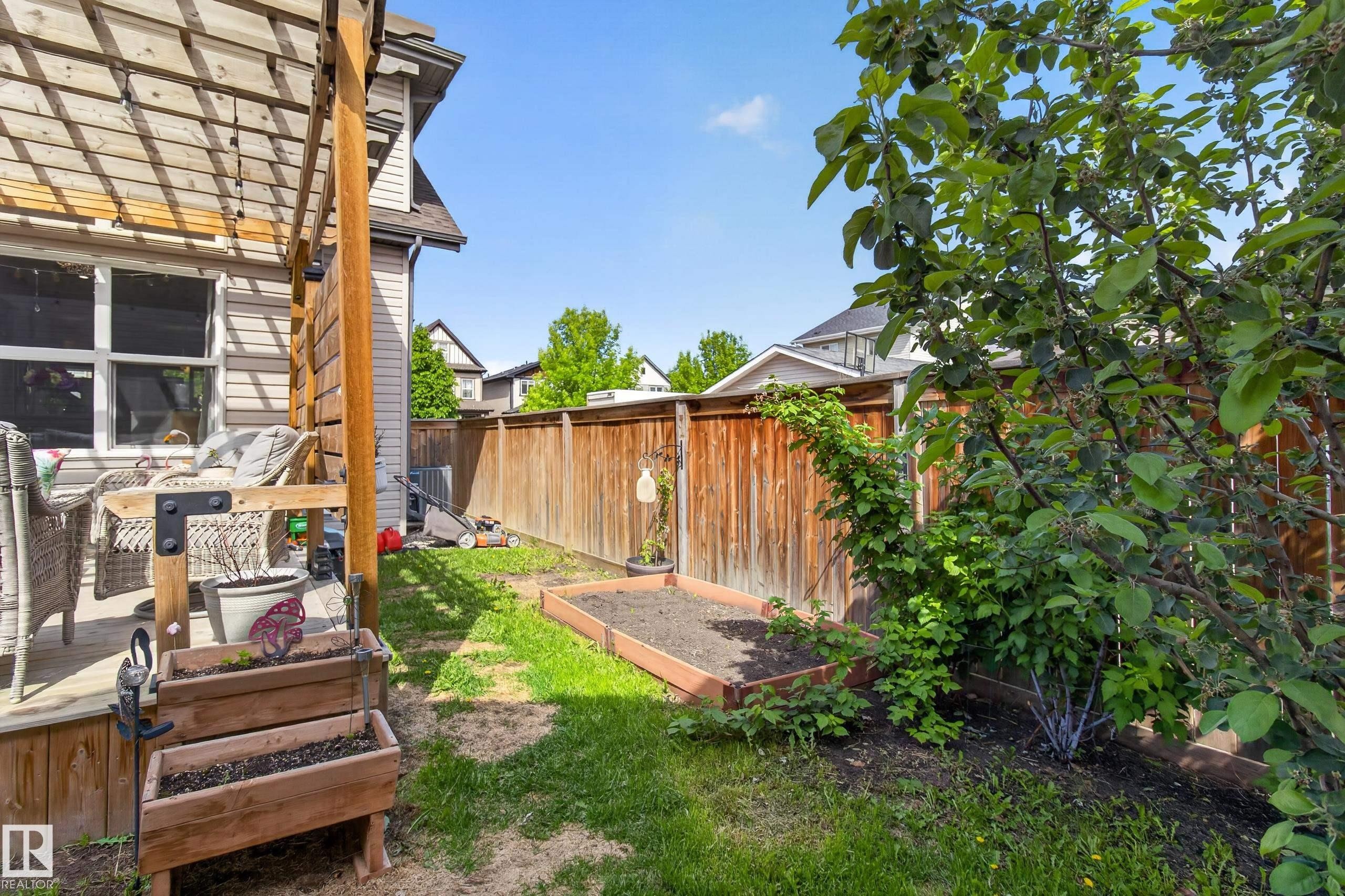 Rear yard with a wooden privacy fence, a raised garden bed, and mature landscaping - 9847 220 Street, Edmonton, AB
