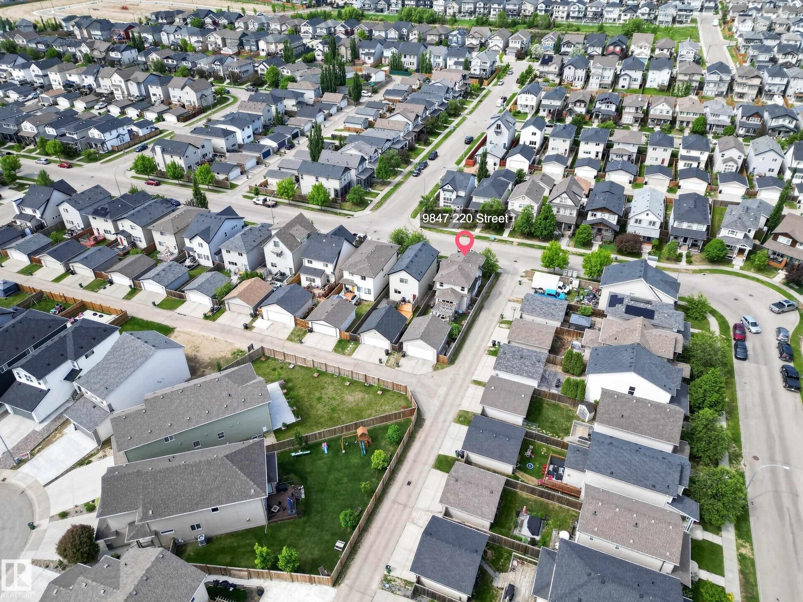 Aerial perspective showcasing a residential neighborhood with uniformly designed homes featuring dark asphalt shingle roofs and light-colored siding - 9847 220 Street, Edmonton, AB