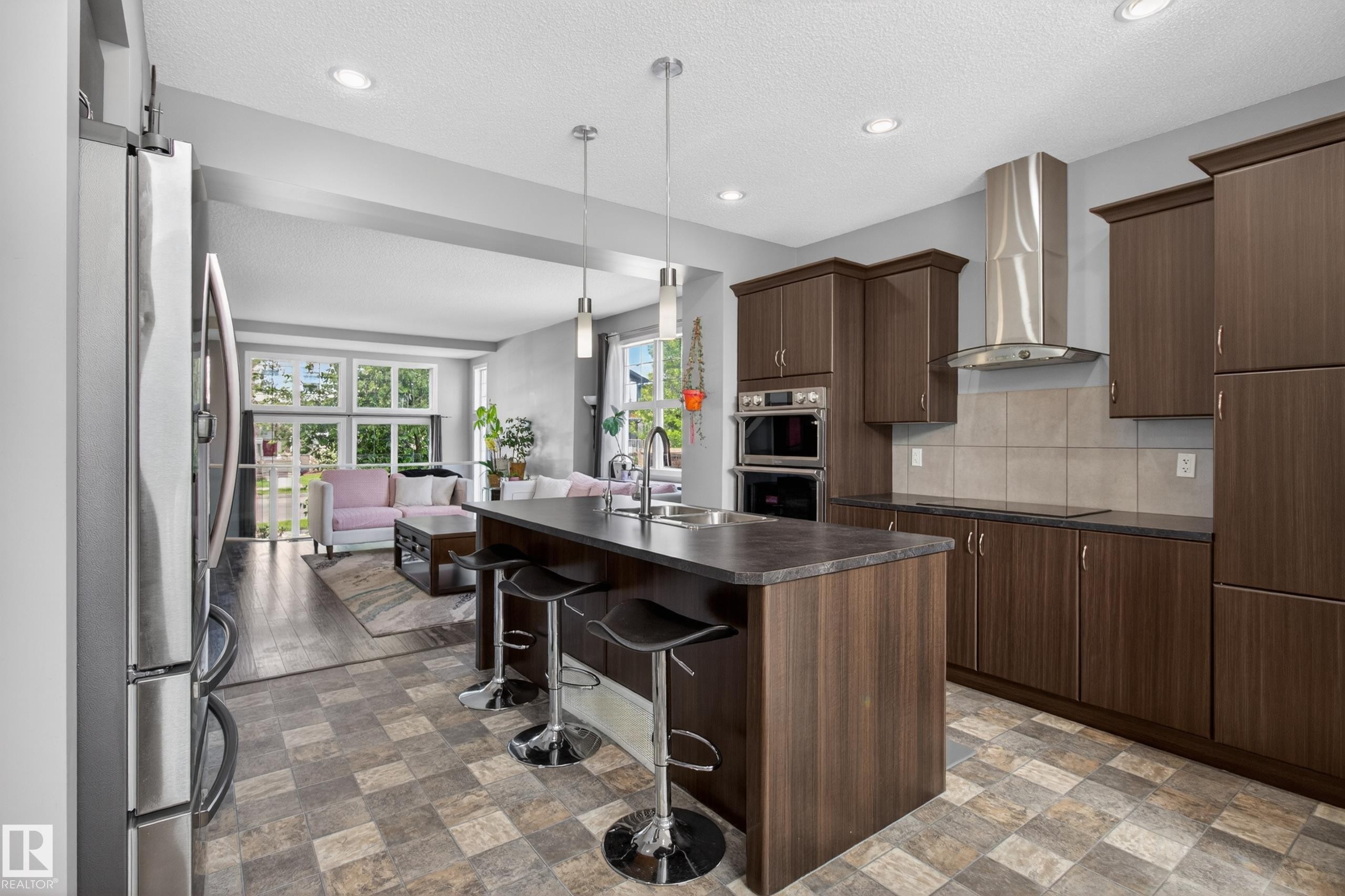 Modern kitchen featuring an island with seating, stainless steel appliances, dark wood-finish cabinetry, and recessed lighting - 9847 220 Street, Edmonton, AB