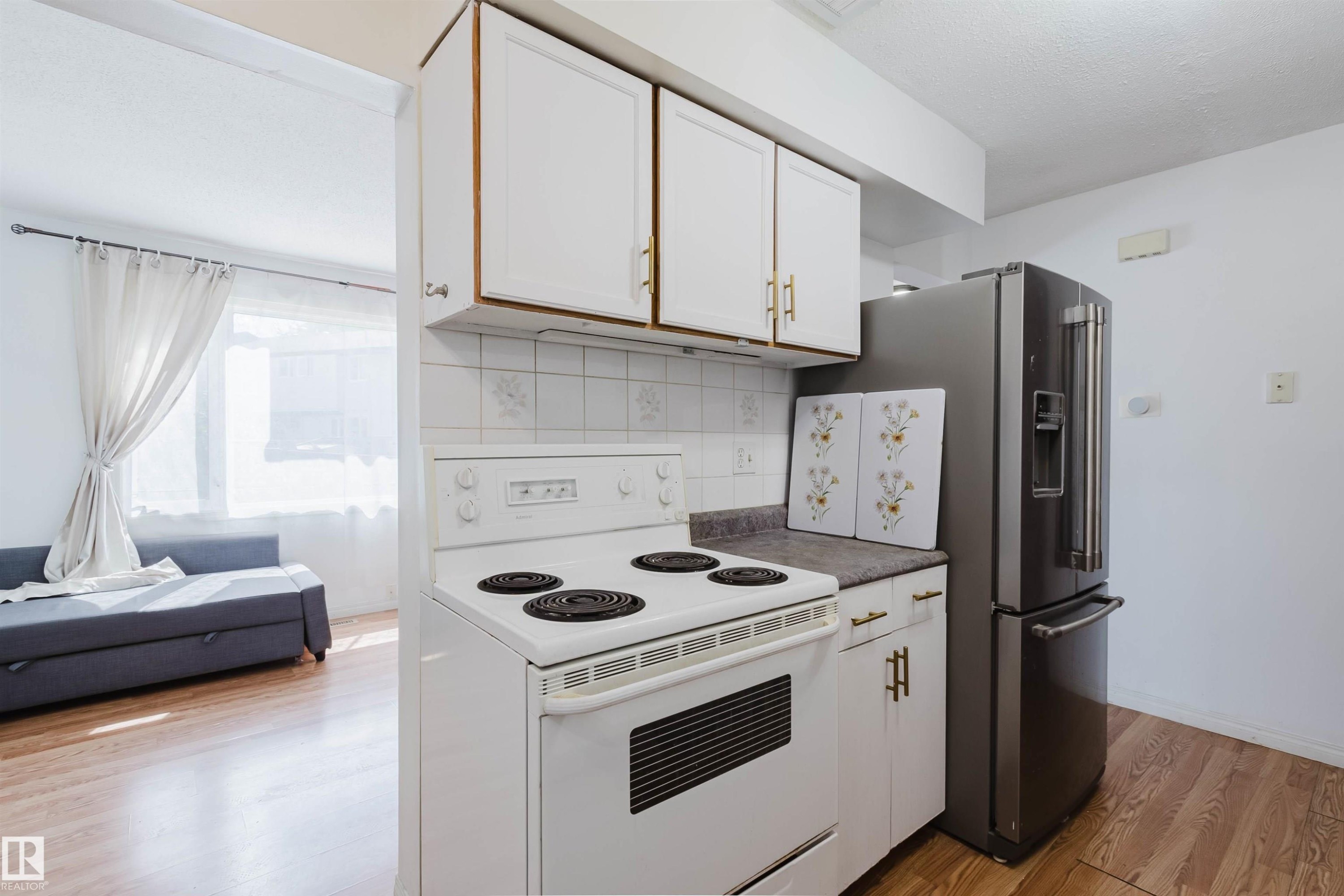 Kitchen featuring wood-finish flooring, white cabinetry with gold-tone hardware, a white electric range, and a stainless steel French door refrigerator - 4 14310 80 Street, Edmonton, AB