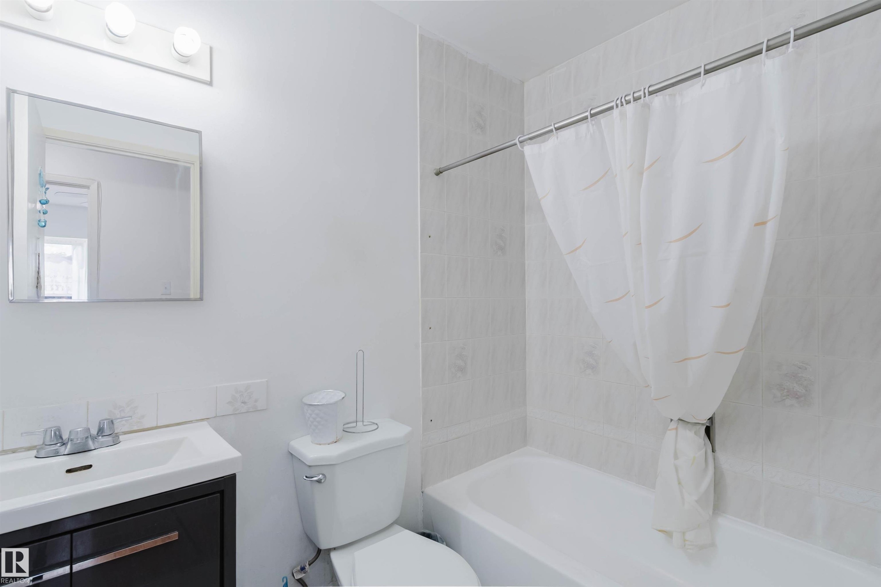 Bathroom featuring a white bathtub, tiled shower surround, and a dark wood-finish vanity with an integrated sink - 4 14310 80 Street, Edmonton, AB