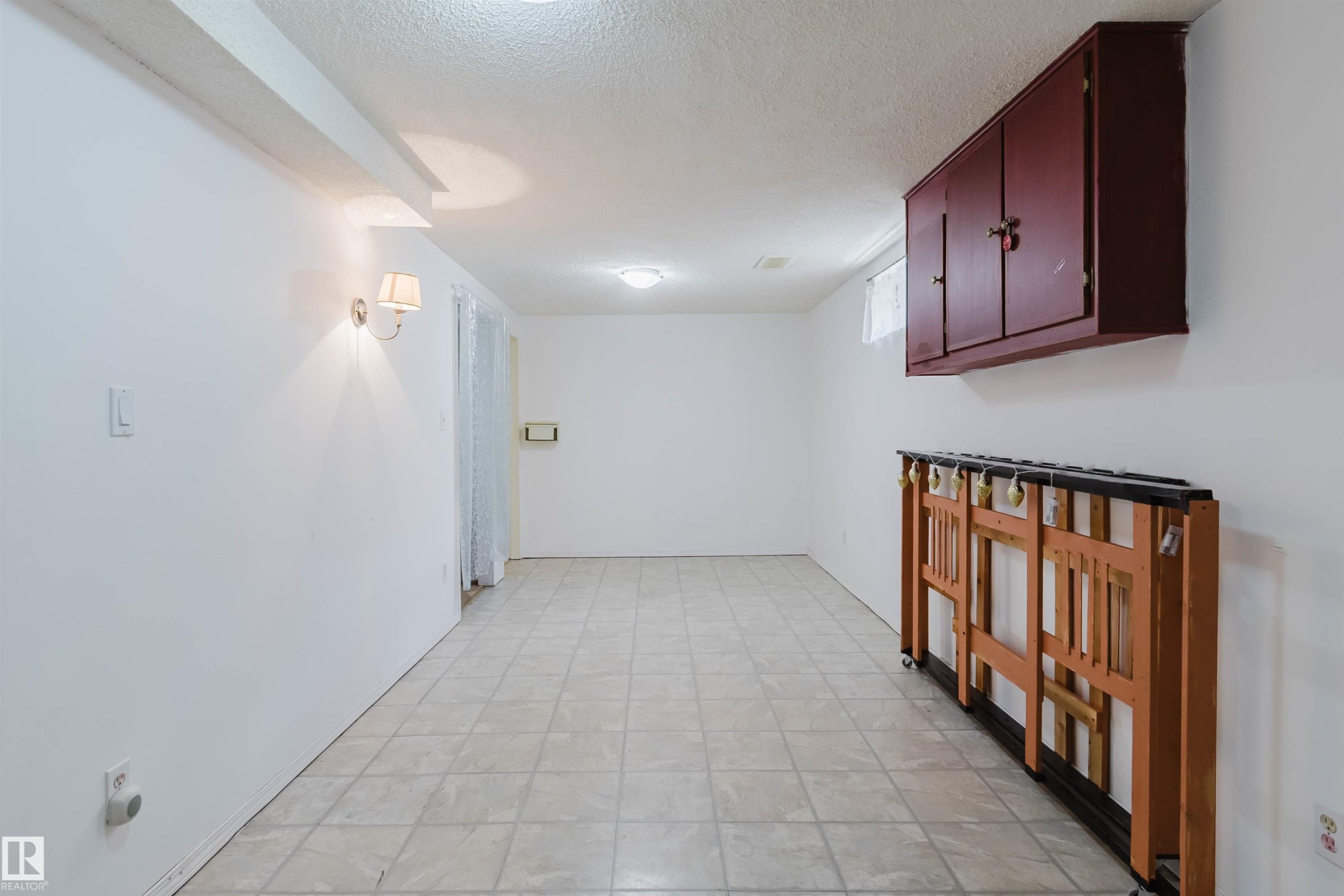 Spacious room featuring light-toned tiled flooring, white painted walls, and a textured ceiling - 4 14310 80 Street, Edmonton, AB