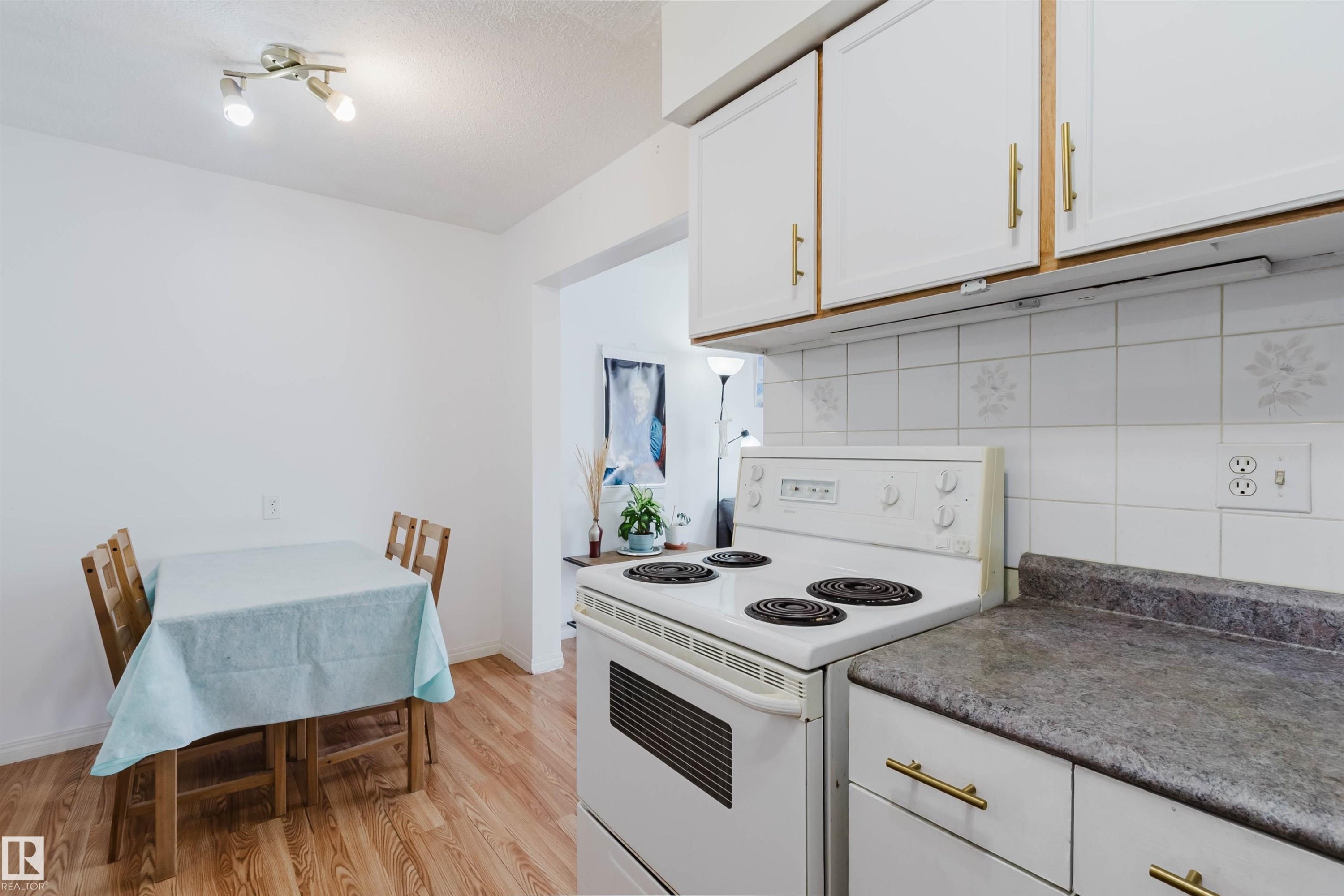 Kitchen featuring white cabinetry with gold-tone hardware, a white electric range, and a gray countertop - 4 14310 80 Street, Edmonton, AB