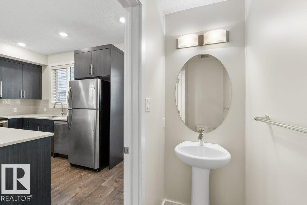 Pedestal sink with an oval mirror, illuminated by a two-light vanity fixture - 125 655 Watt Boulevard, Edmonton, AB