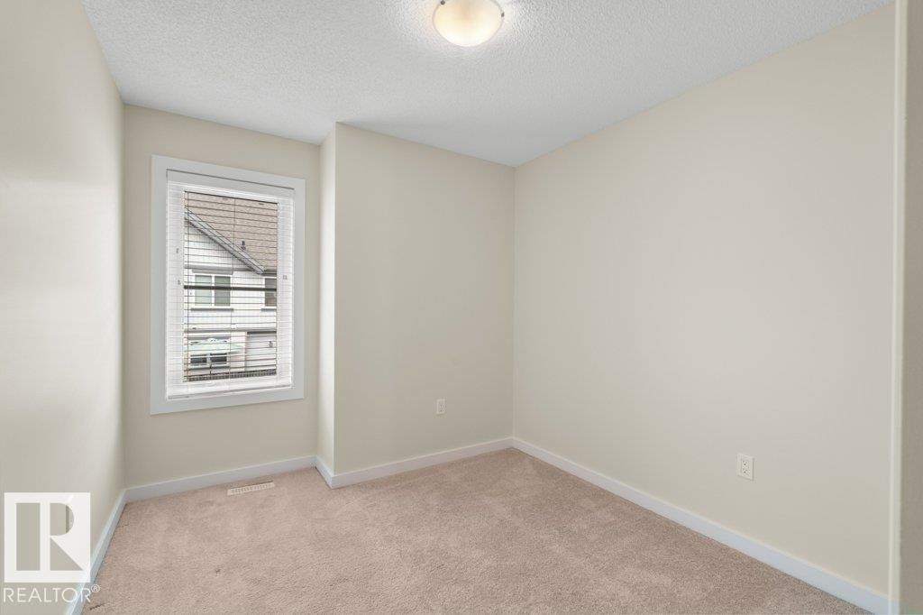 Neutral-toned room featuring a single window with blinds, light beige carpeting, white baseboards, and a semi-flush mount ceiling light fixture - 125 655 Watt Boulevard, Edmonton, AB