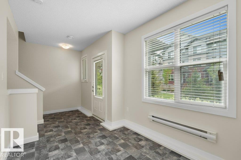 Entryway featuring patterned tile flooring, a half-glass entry door with vertical blinds, a large window with horizontal blinds, and baseboard heating - 125 655 Watt Boulevard, Edmonton, AB
