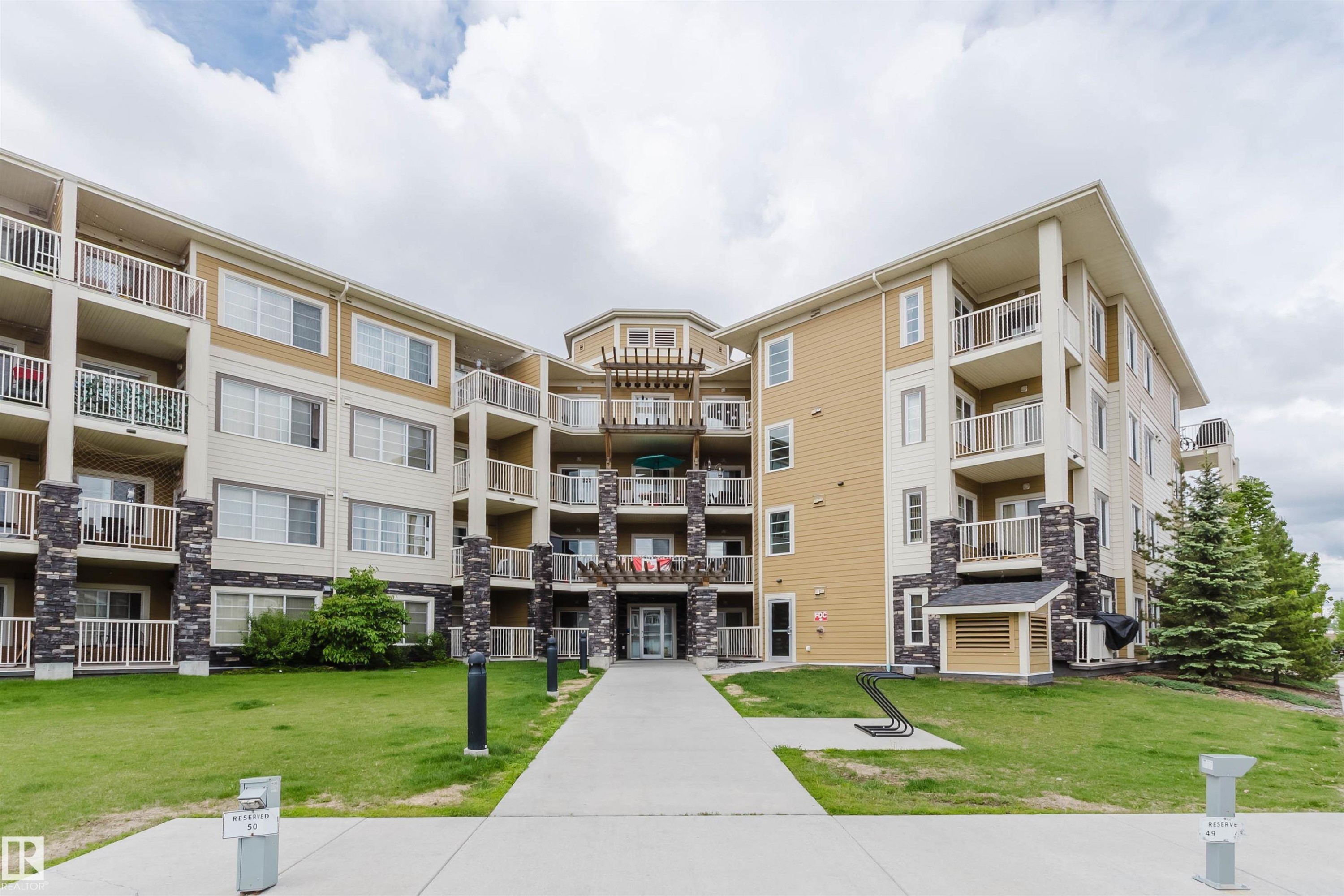 Multi-story building exterior featuring a neutral color palette, stone accents, and multiple private balconies with white railings - 402 3670 139 Avenue, Edmonton, AB
