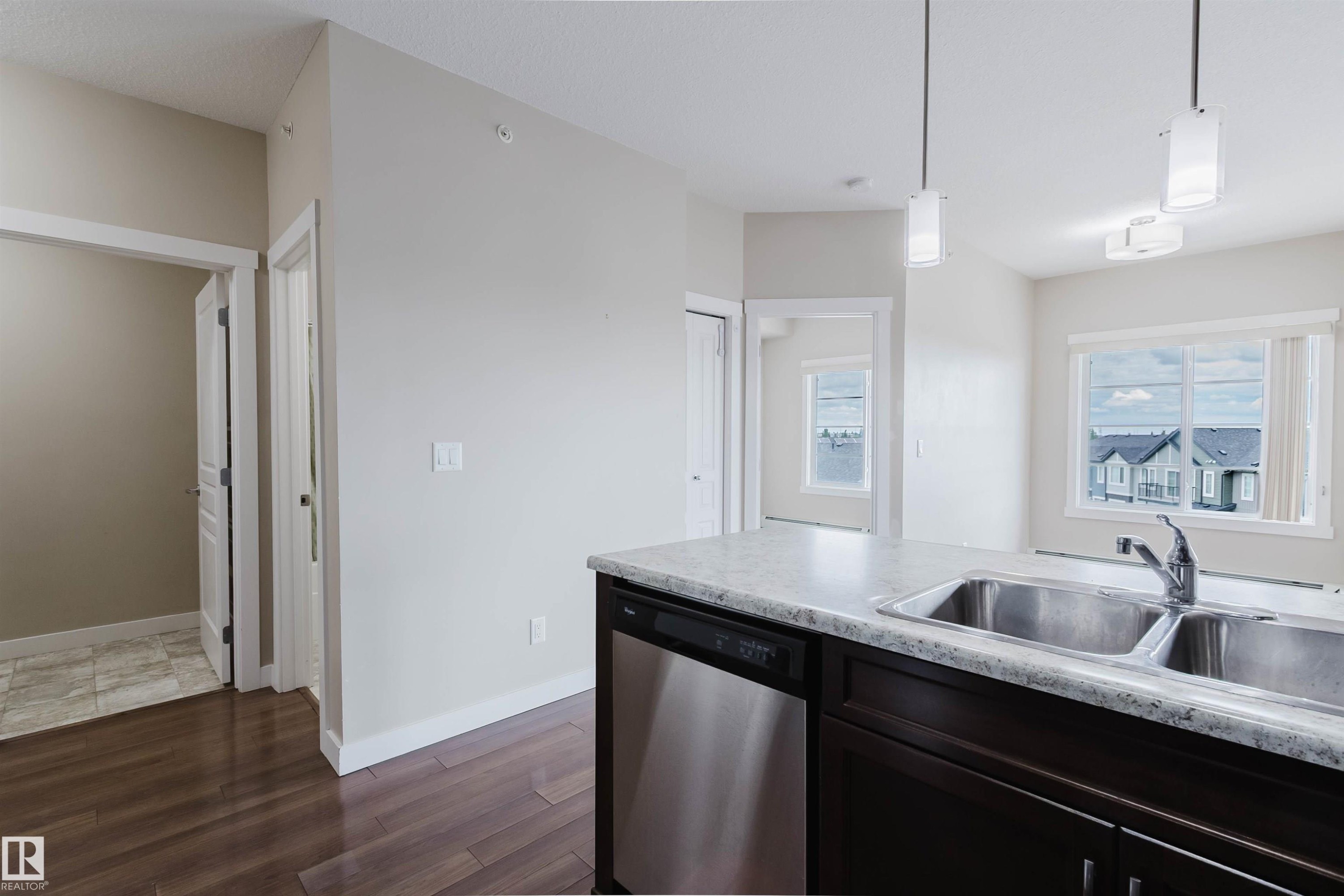 Kitchen island featuring a double basin stainless steel sink, stainless steel dishwasher, and dark wood cabinetry - 402 3670 139 Avenue, Edmonton, AB