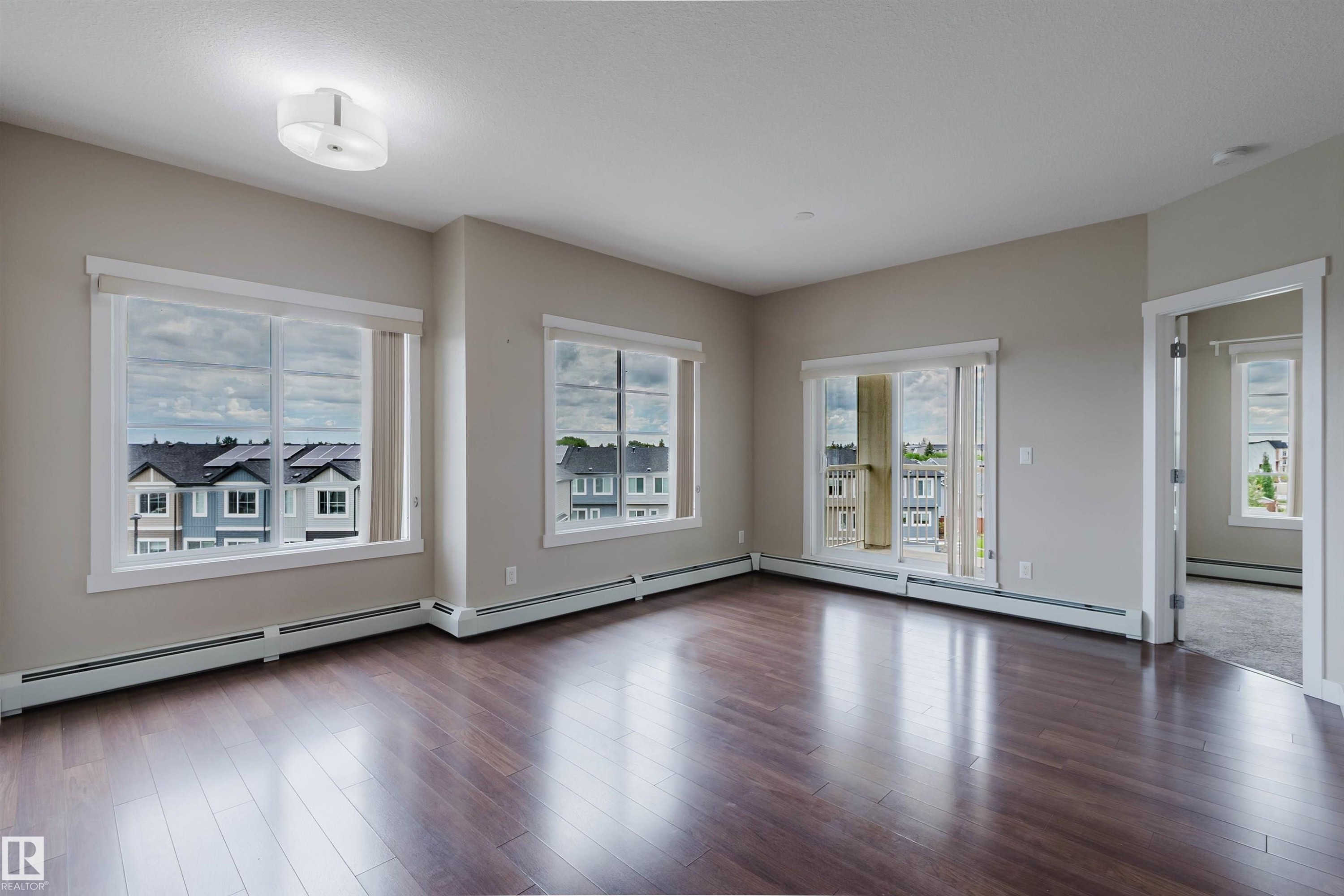 Spacious interior featuring wood-finish flooring, light neutral wall paint, white trim, and a ceiling-mounted light fixture - 402 3670 139 Avenue, Edmonton, AB