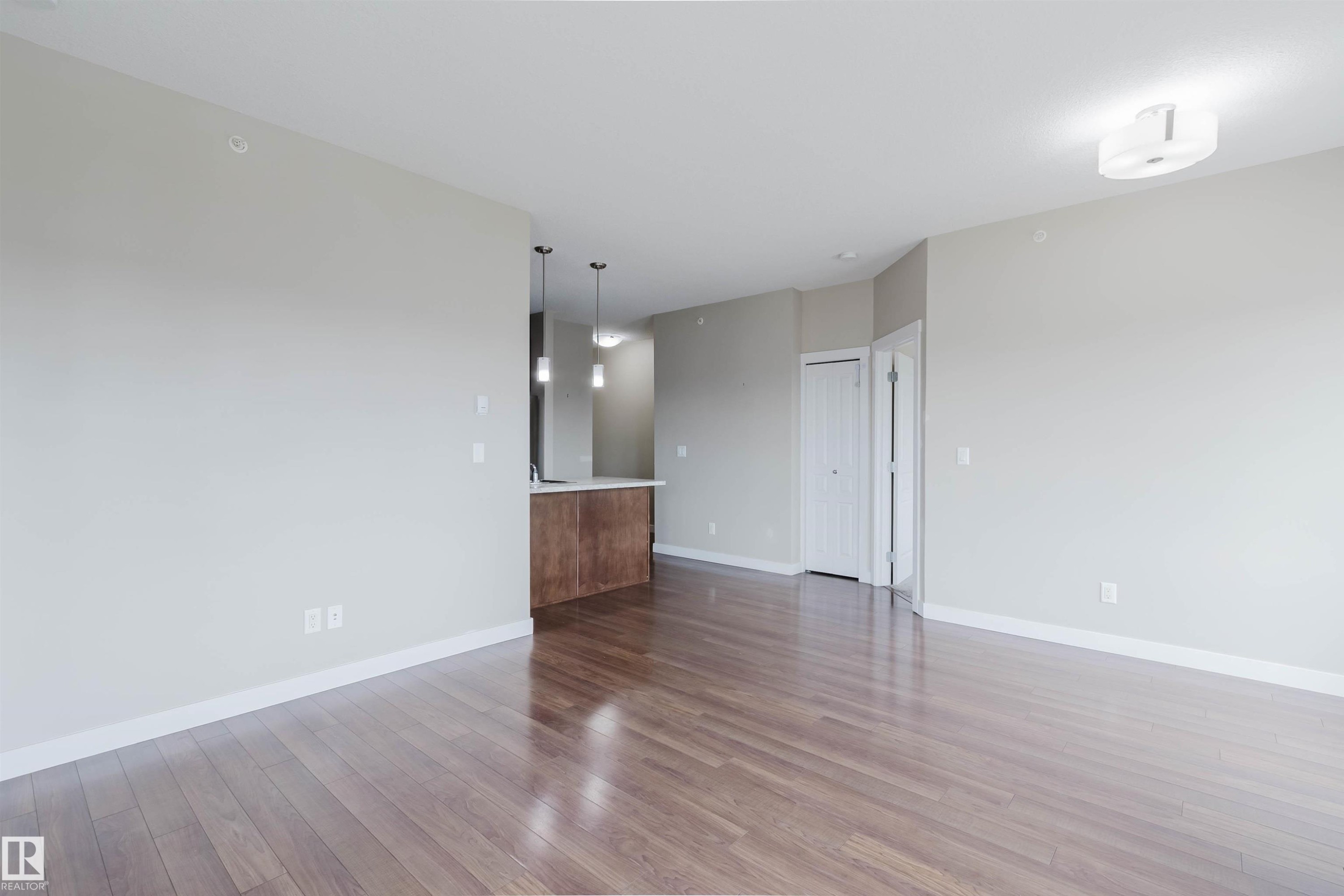 Open-concept living space featuring wood-finish flooring, a kitchen island with a light-toned countertop, and two pendant lights - 402 3670 139 Avenue, Edmonton, AB