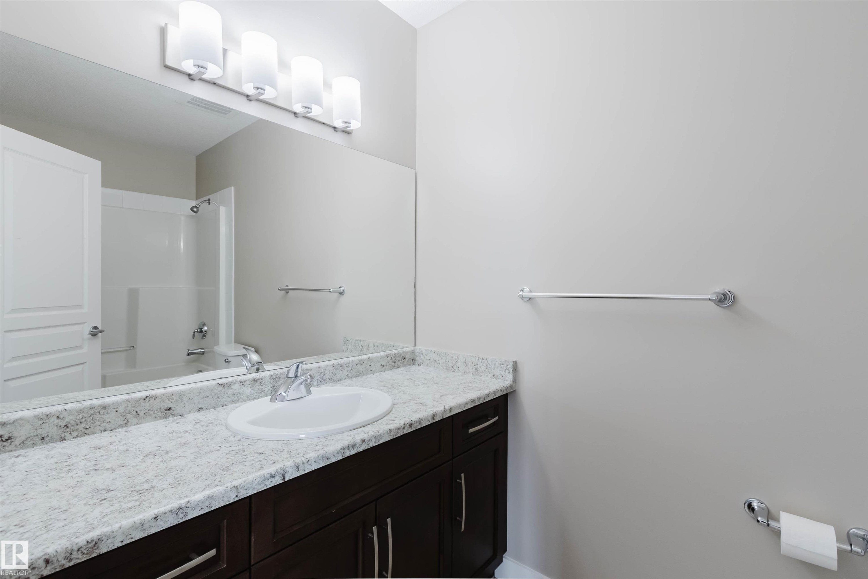 Bathroom vanity featuring a speckled countertop, undermount sink, and dark wood cabinetry - 402 3670 139 Avenue, Edmonton, AB