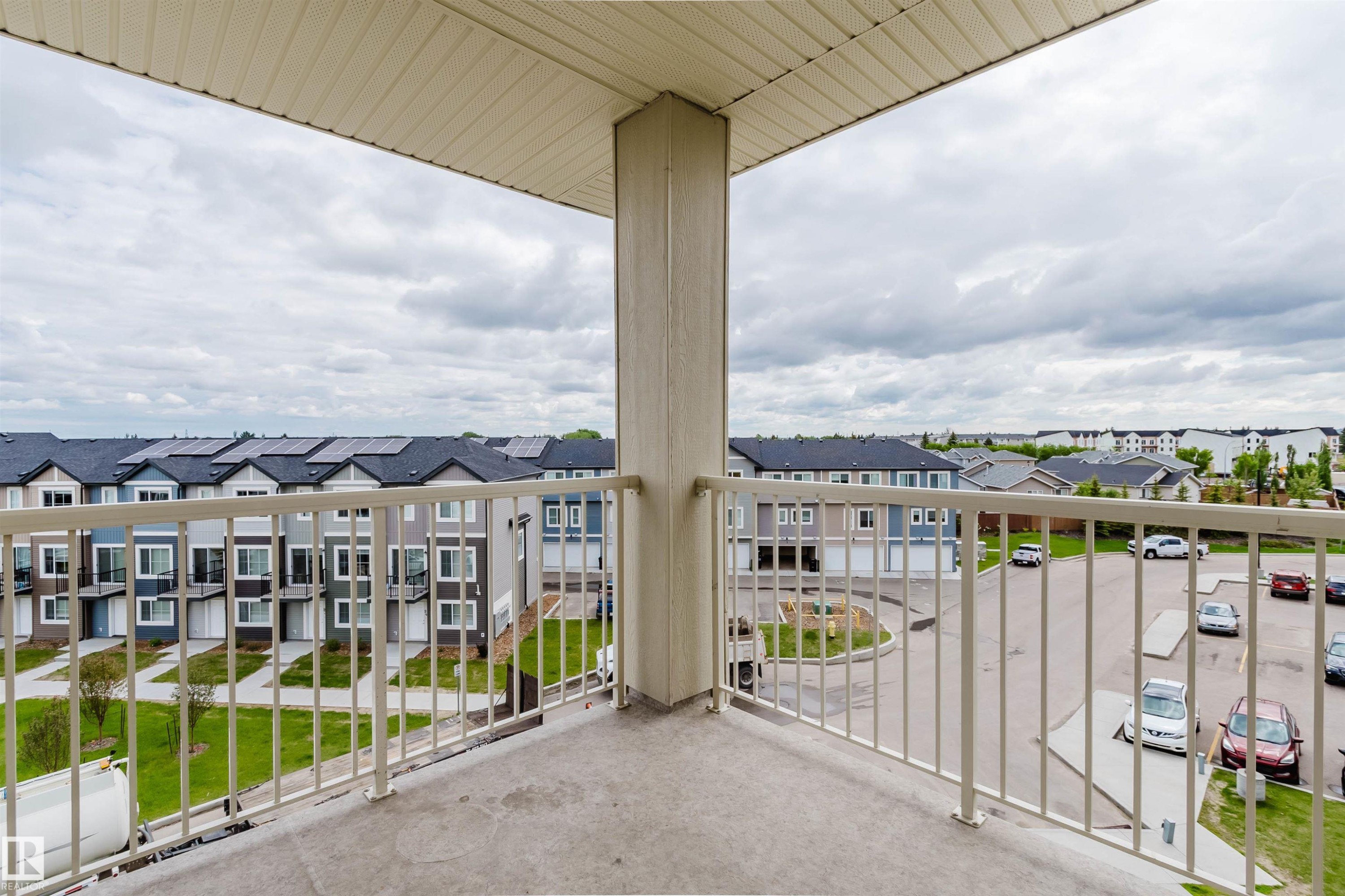 Concrete balcony with cream-colored metal railing, overlooking a residential area with varied housing styles and community green spaces - 402 3670 139 Avenue, Edmonton, AB