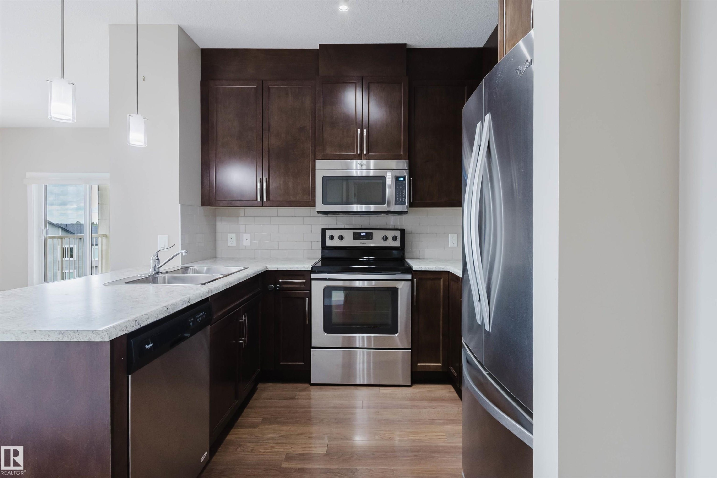 Modern kitchen featuring rich, dark wood cabinetry, stainless steel appliances, and wood-finish flooring - 402 3670 139 Avenue, Edmonton, AB