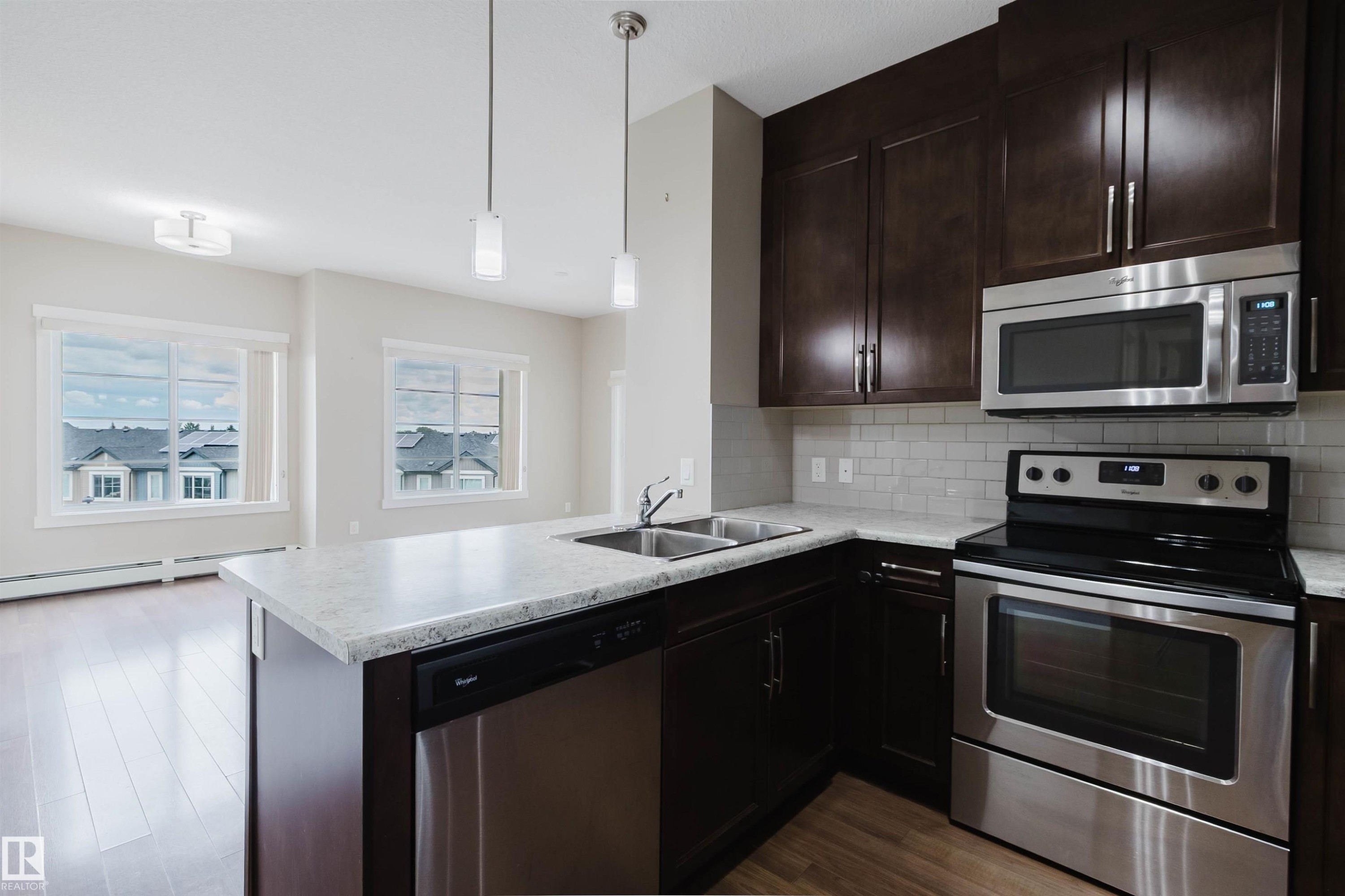 Contemporary kitchen featuring dark wood cabinetry, stainless steel appliances, a subway tile backsplash, and light-toned countertops - 402 3670 139 Avenue, Edmonton, AB