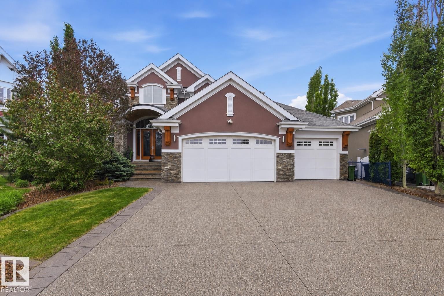 Stucco and stone facade with a decorative arched entry, featuring a multi-car aggregate driveway with paver edging, integrated garage doors with window accents, and mature landscaping - 9003 16 Avenue Sw, Edmonton, AB - Outdoor With Facade