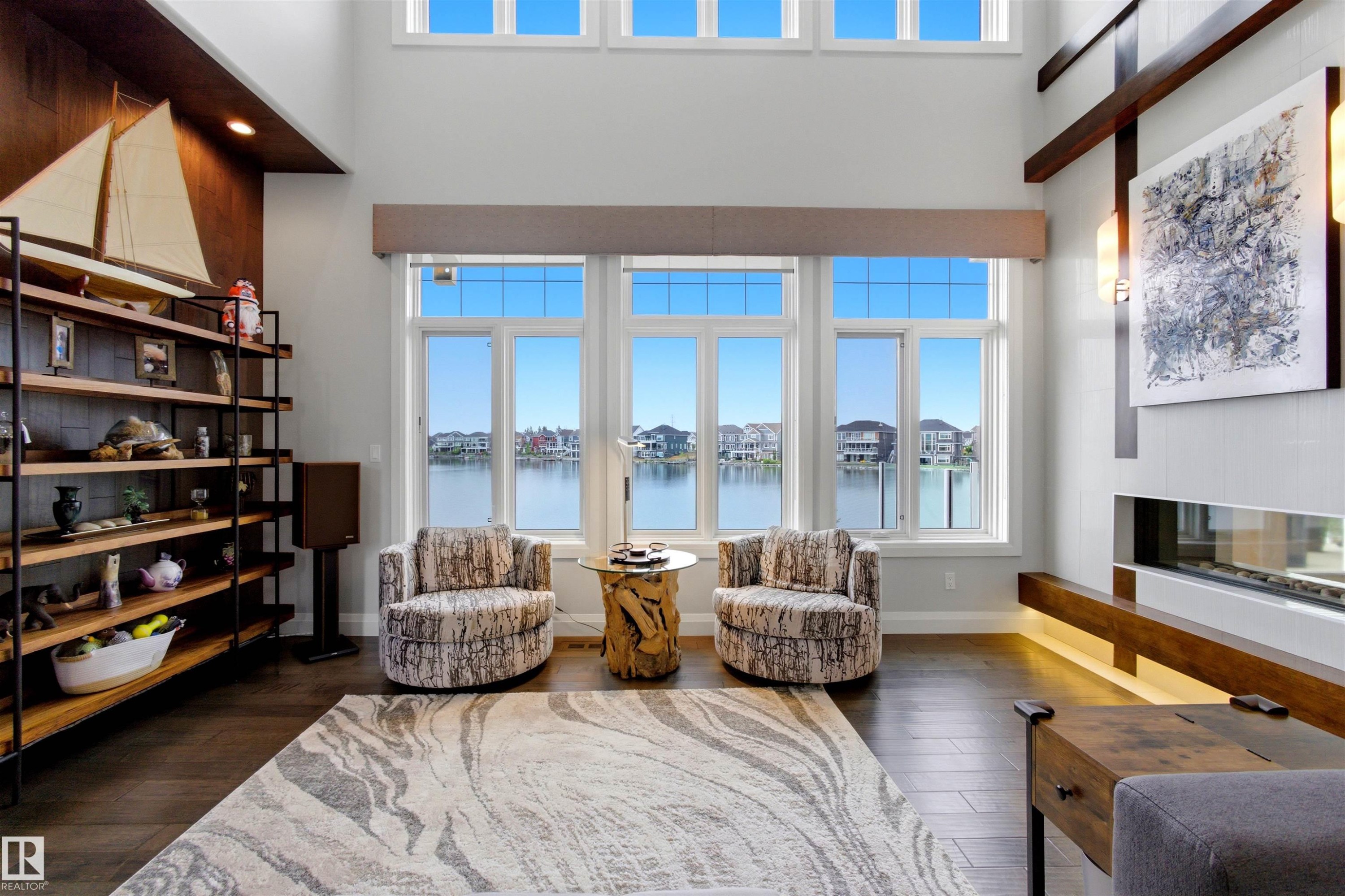 Living space featuring a wall of expansive windows overlooking a body of water, alongside upper transom windows - 9003 16 Avenue Sw, Edmonton, AB - Indoor Photo Showing Living Room With Fireplace