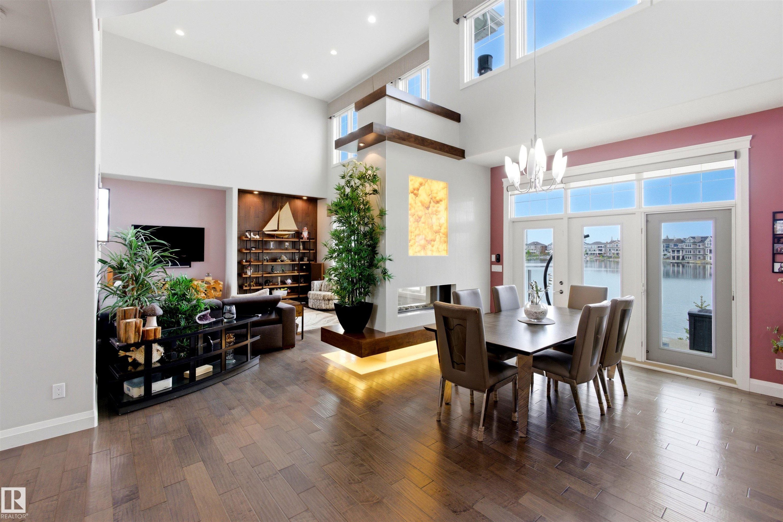Spacious interior featuring high ceilings, wood-finish flooring, a contemporary fireplace with integrated lighting, and extensive windows with water views - 9003 16 Avenue Sw, Edmonton, AB - Indoor Photo Showing Dining Room
