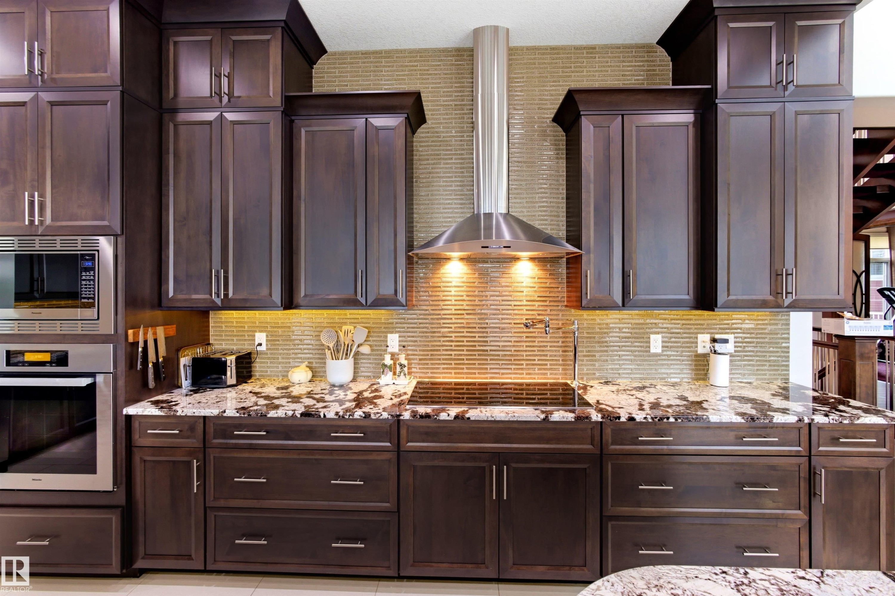 Kitchen featuring dark wood cabinetry, stainless steel appliances, a mosaic tile backsplash, and stone countertops - 9003 16 Avenue Sw, Edmonton, AB - Indoor Photo Showing Kitchen With Upgraded Kitchen