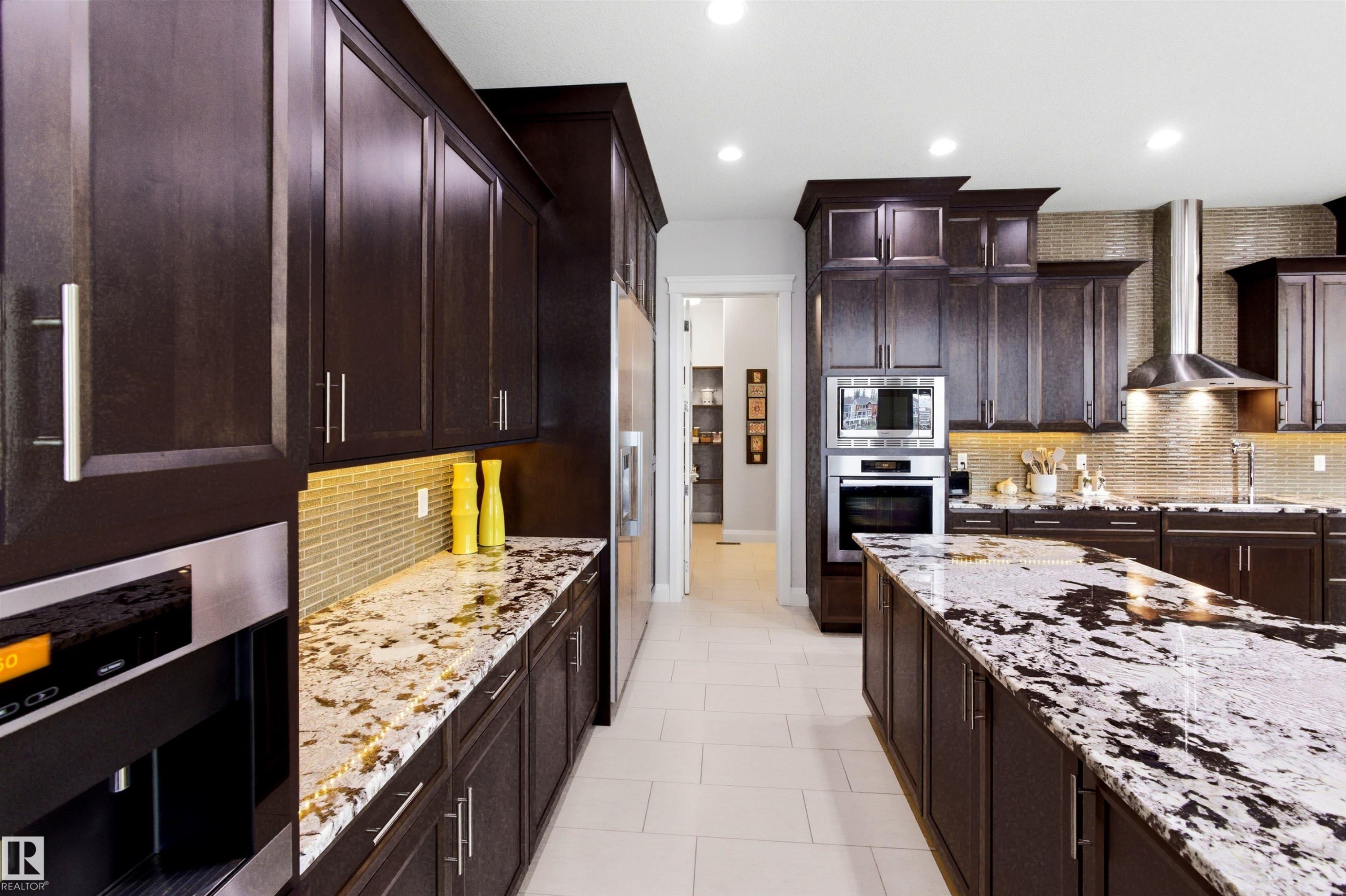 Contemporary kitchen featuring dark wood cabinetry, light-toned tile flooring, and integrated stainless steel appliances including a built-in oven and microwave - 9003 16 Avenue Sw, Edmonton, AB - Indoor Photo Showing Kitchen With Upgraded Kitchen
