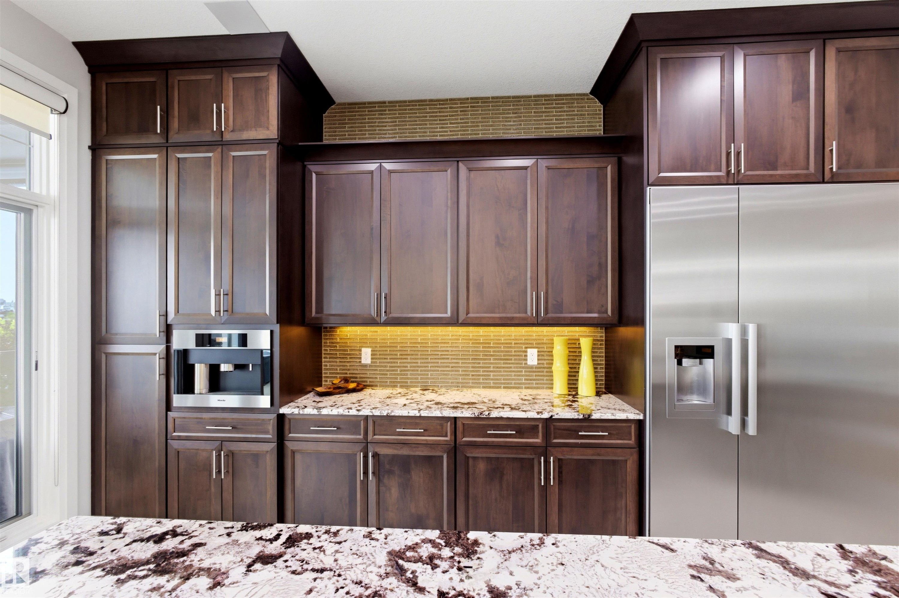 Integrated kitchen featuring rich wood cabinetry, stainless steel appliances, a built-in coffee maker, under-cabinet lighting, and a linear mosaic tile backsplash - 9003 16 Avenue Sw, Edmonton, AB - Indoor Photo Showing Kitchen