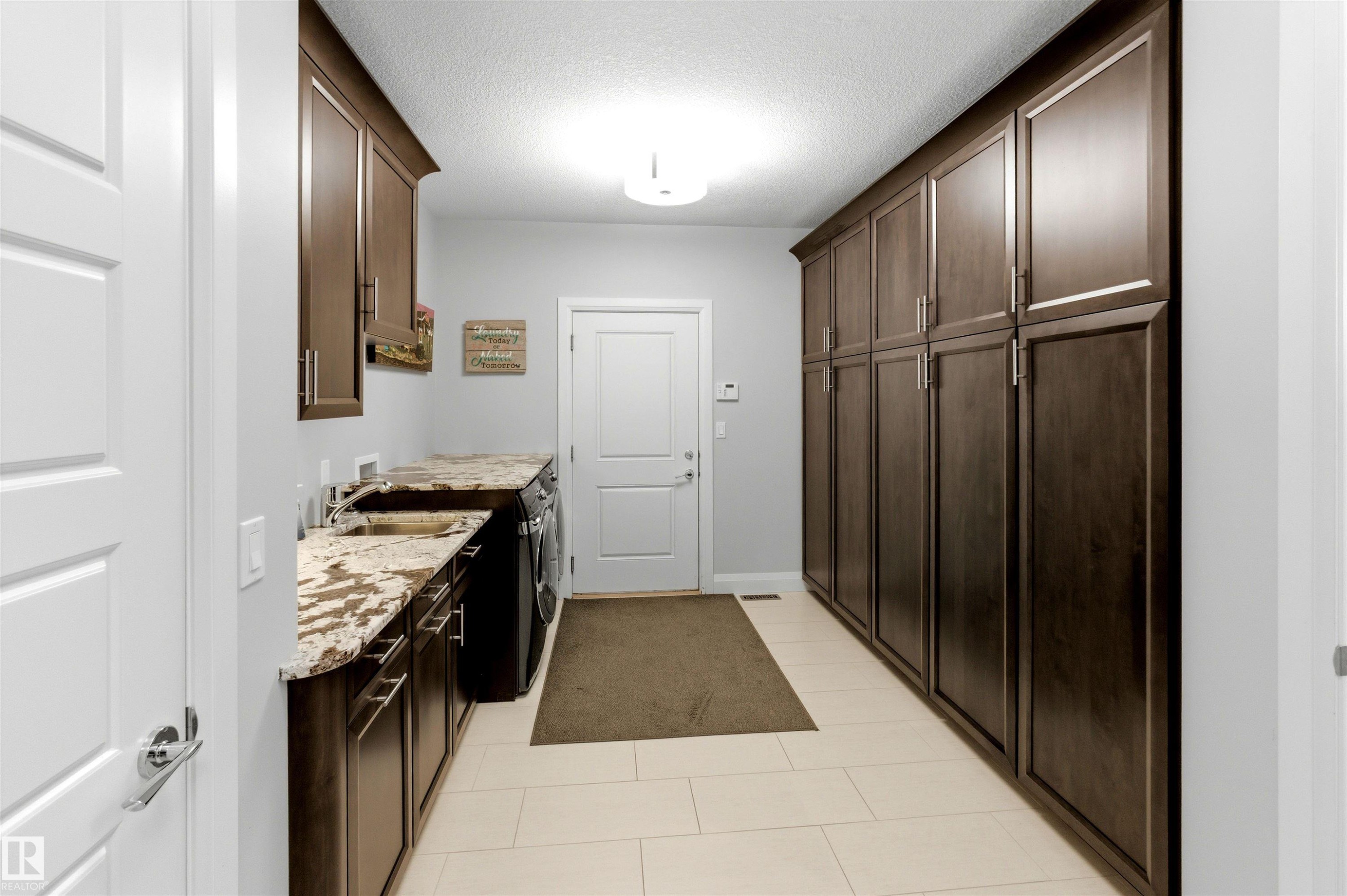 Utility room featuring extensive dark wood cabinetry, light-toned tile flooring, and a countertop with integrated sink - 9003 16 Avenue Sw, Edmonton, AB - Indoor