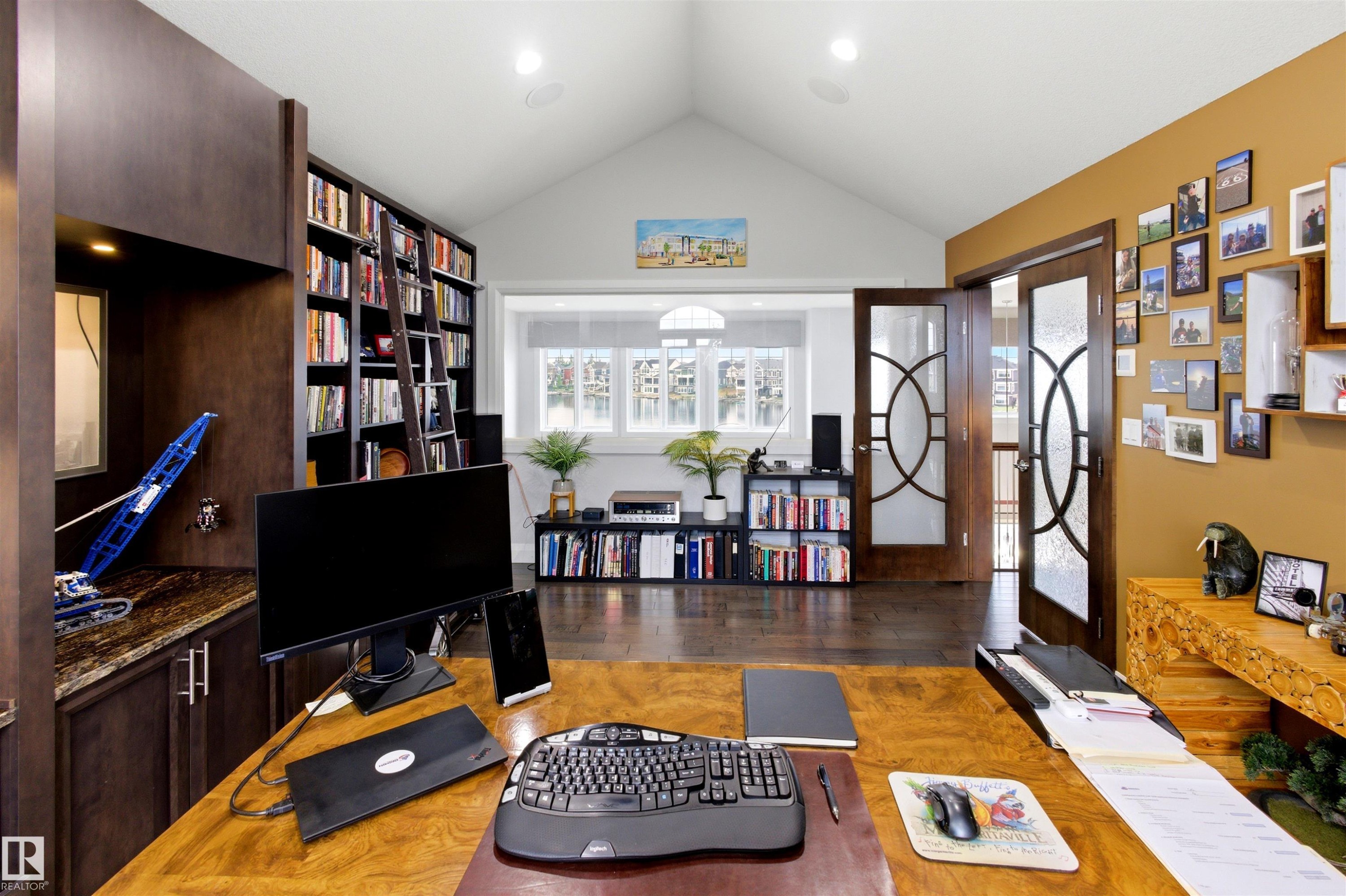 Home office featuring a built-in wood-finish desk with a granite countertop, extensive shelving with a rolling ladder, and vaulted ceilings - 9003 16 Avenue Sw, Edmonton, AB - Indoor Photo Showing Other Room