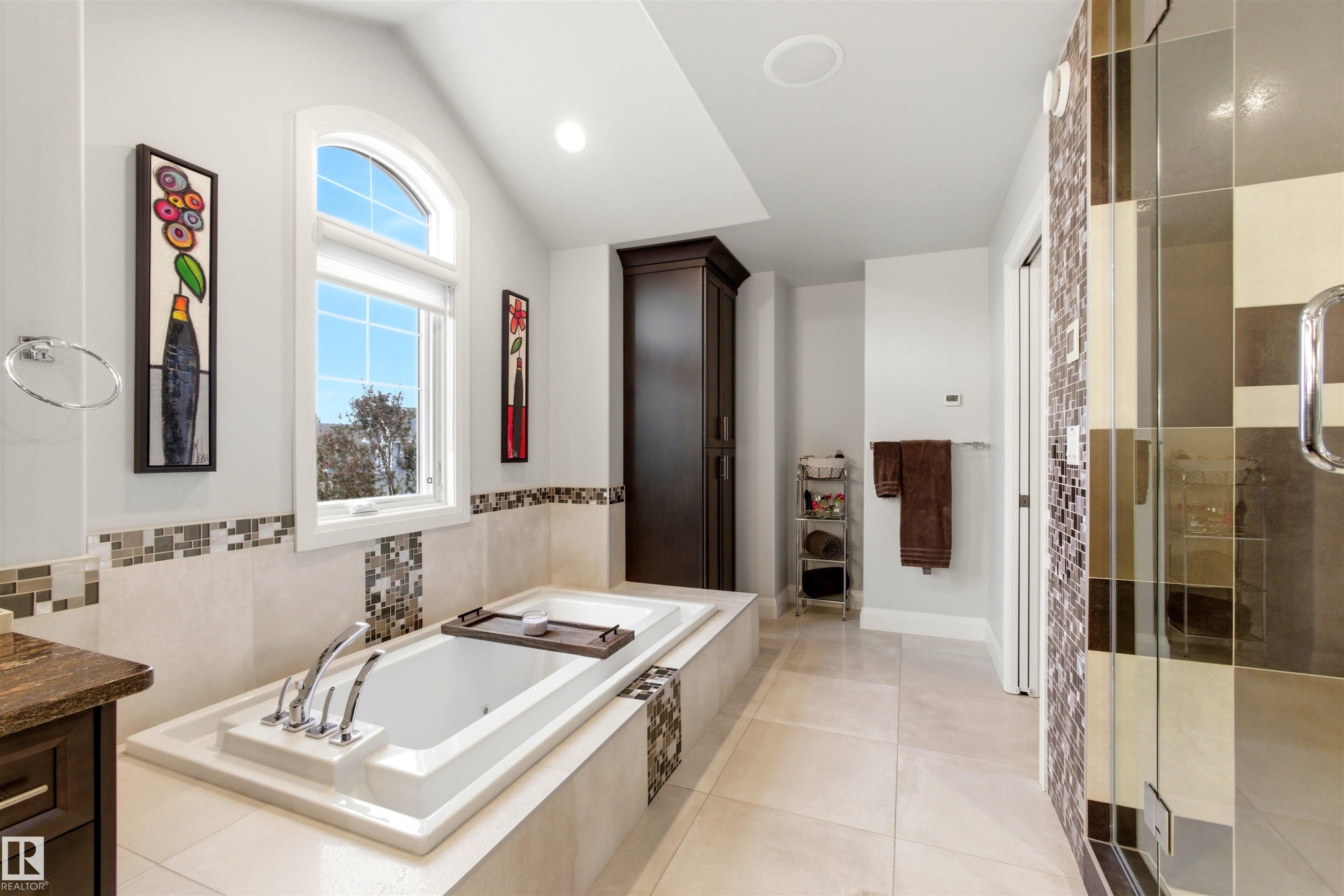 Soaking tub with deck-mounted chrome fixtures, set within a tiled surround featuring mosaic accents - 9003 16 Avenue Sw, Edmonton, AB - Indoor Photo Showing Bathroom